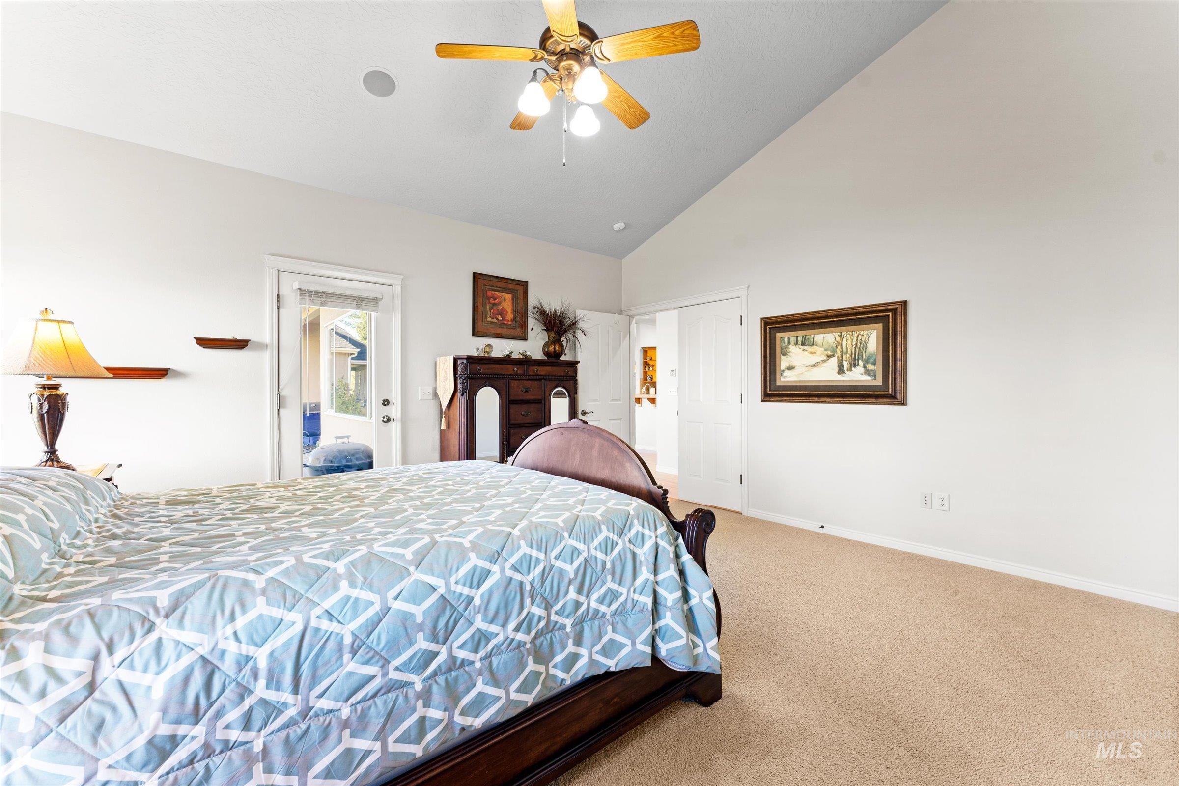 Carpeted bedroom with a ceiling fan and high vaulted ceiling
