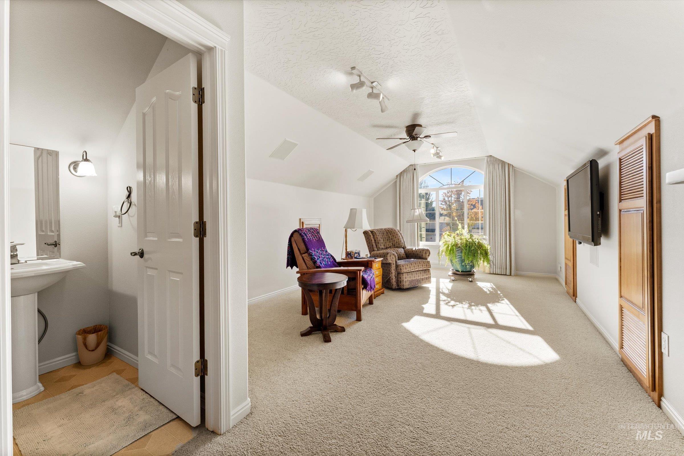 Living area with vaulted ceiling, light colored carpet, a textured ceiling, and a ceiling fan