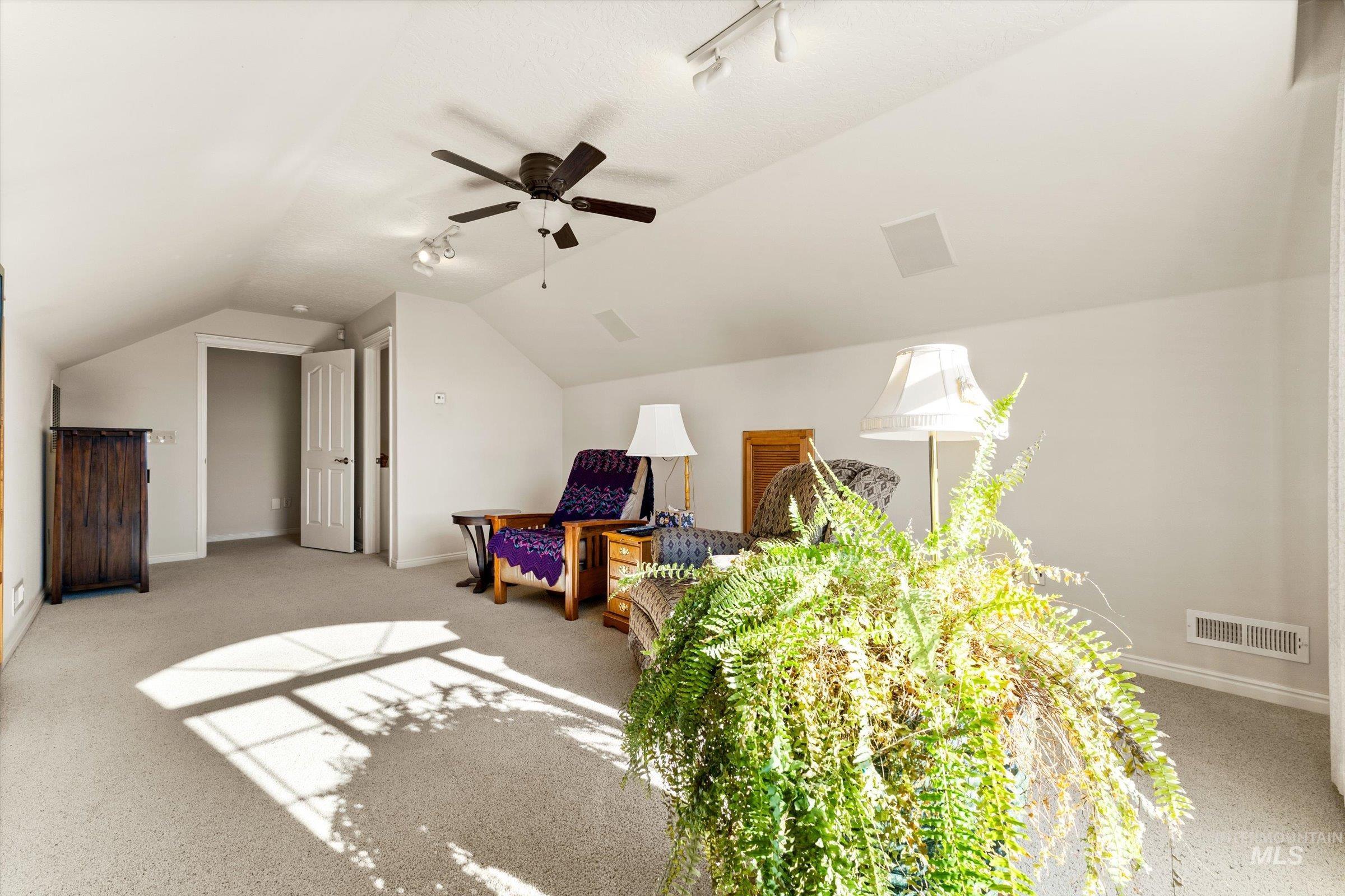 Bedroom featuring vaulted ceiling, rail lighting, light carpet, and a ceiling fan