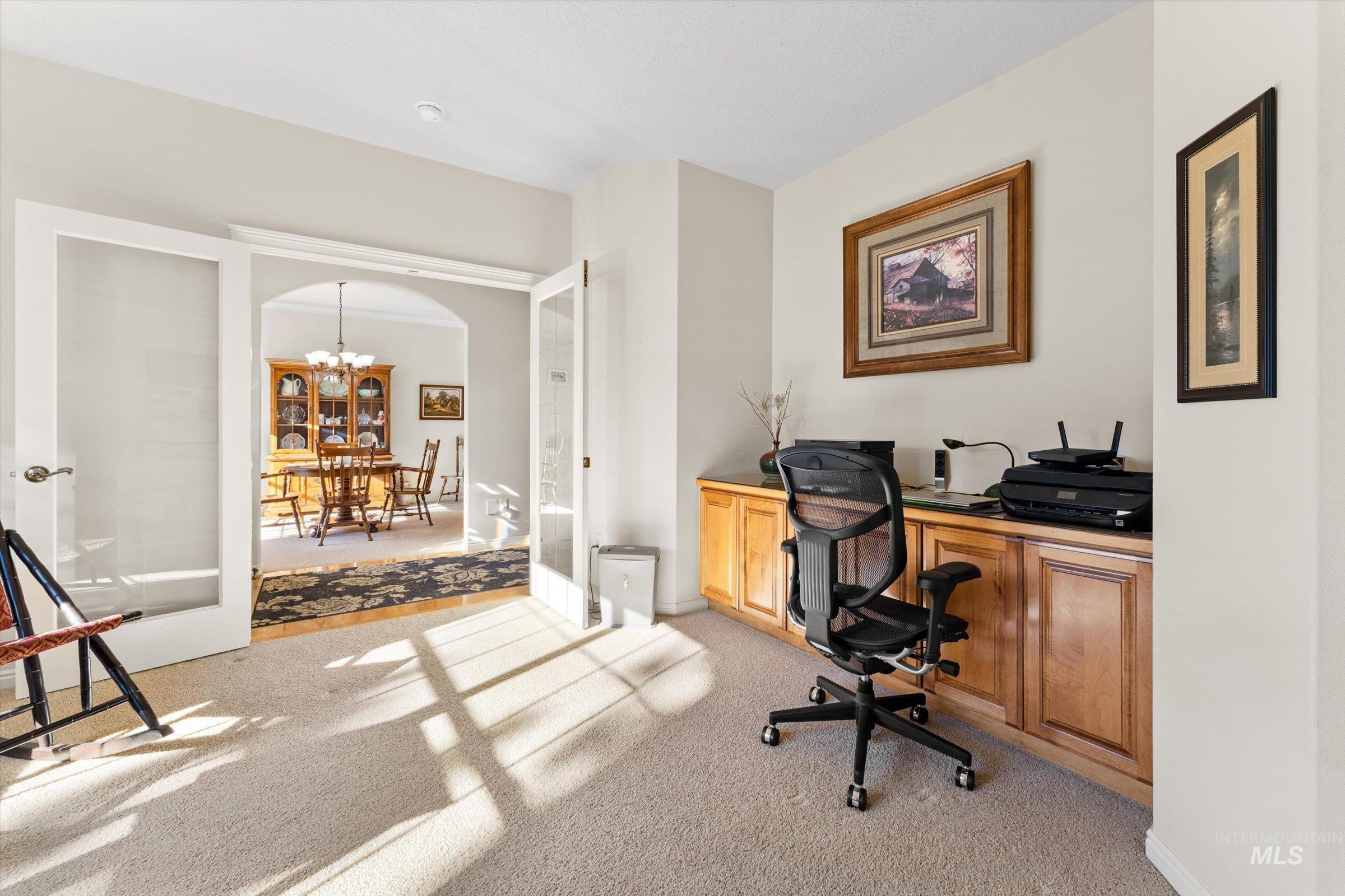 Office area featuring light colored carpet, french doors, a chandelier, and arched walkways