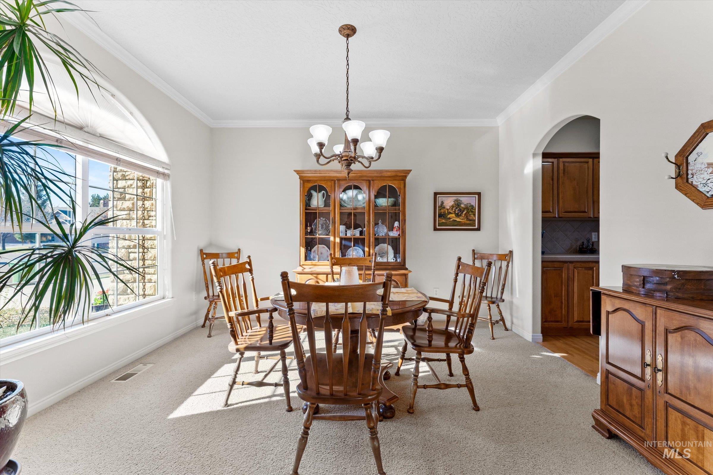 Dining room featuring crown molding, light colored carpet, a chandelier, and arched walkways