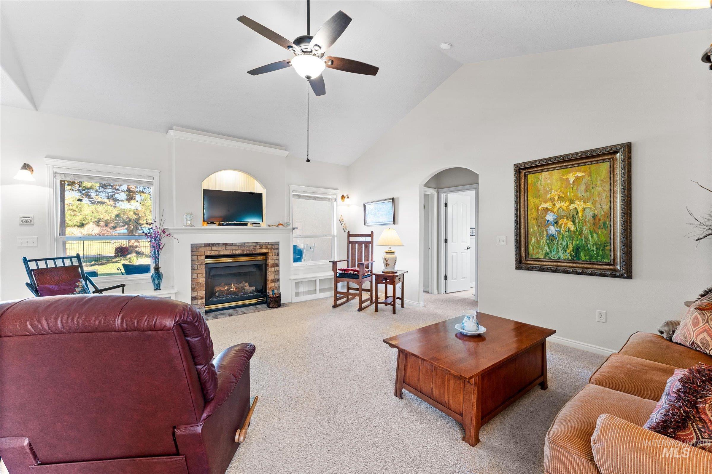 Carpeted living area featuring high vaulted ceiling, arched walkways, a stone fireplace, and a ceiling fan