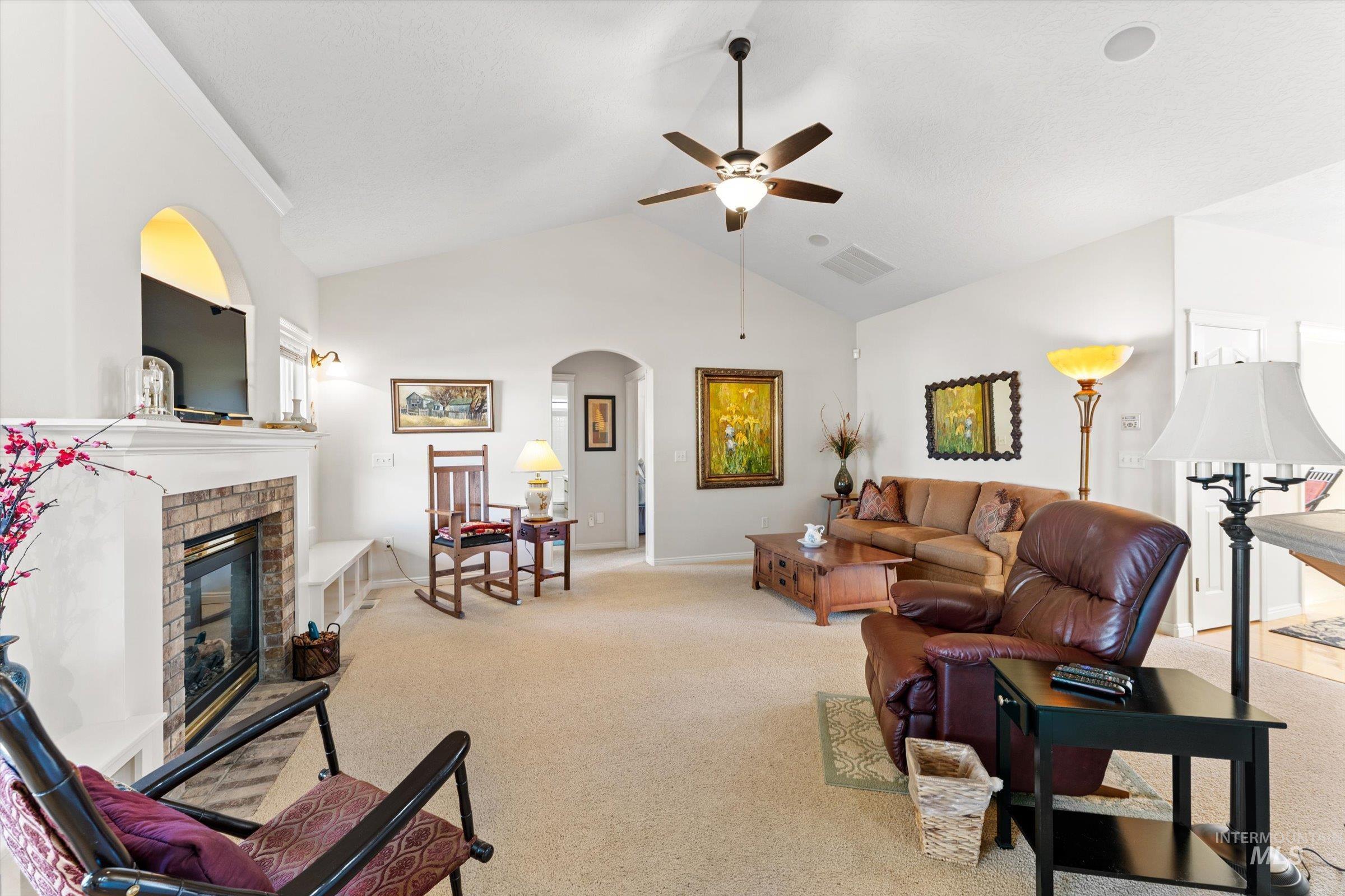 Carpeted living room featuring a brick fireplace, arched walkways, high vaulted ceiling, and a ceiling fan