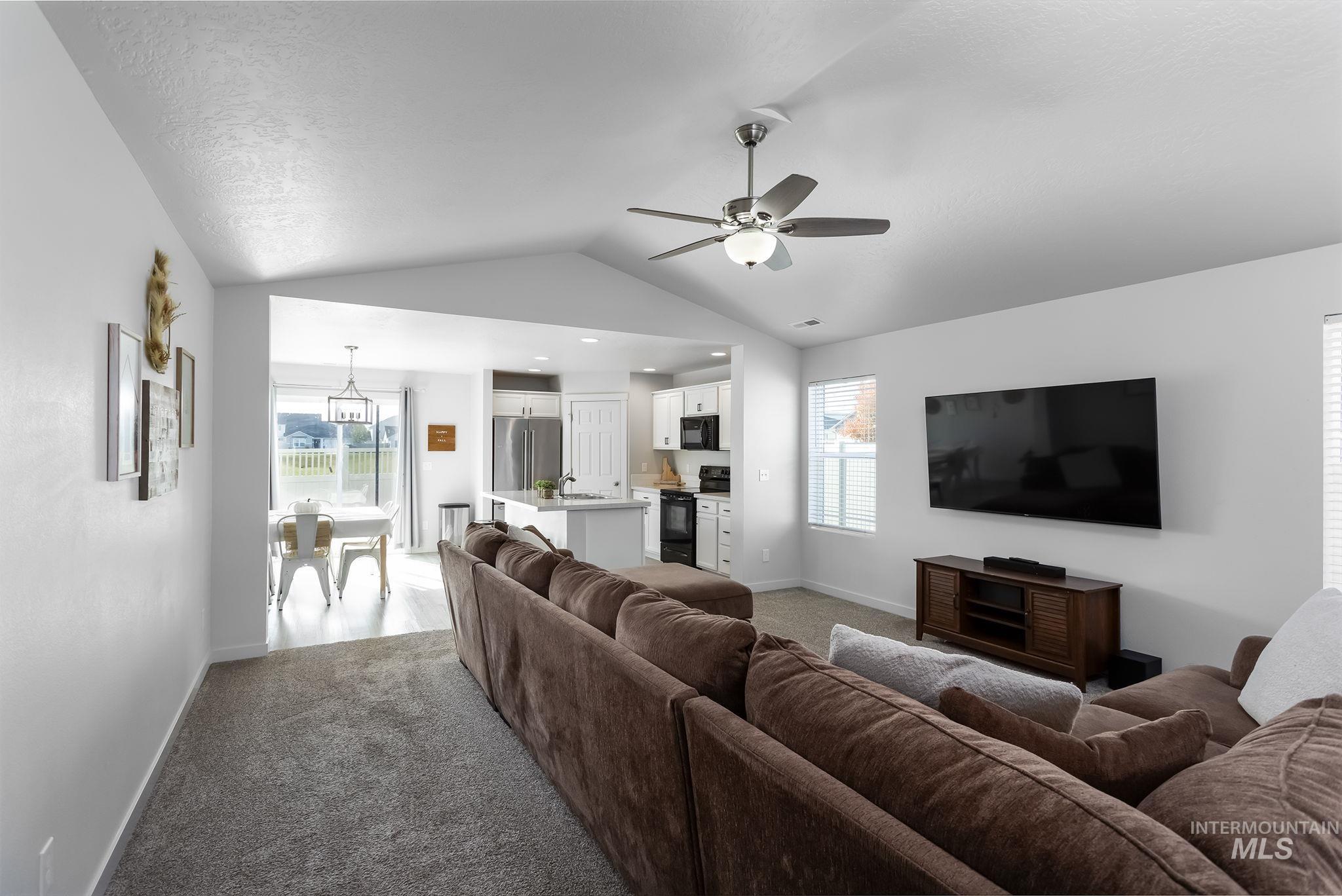 Living room with healthy amount of natural light, vaulted ceiling, carpet floors, and ceiling fan