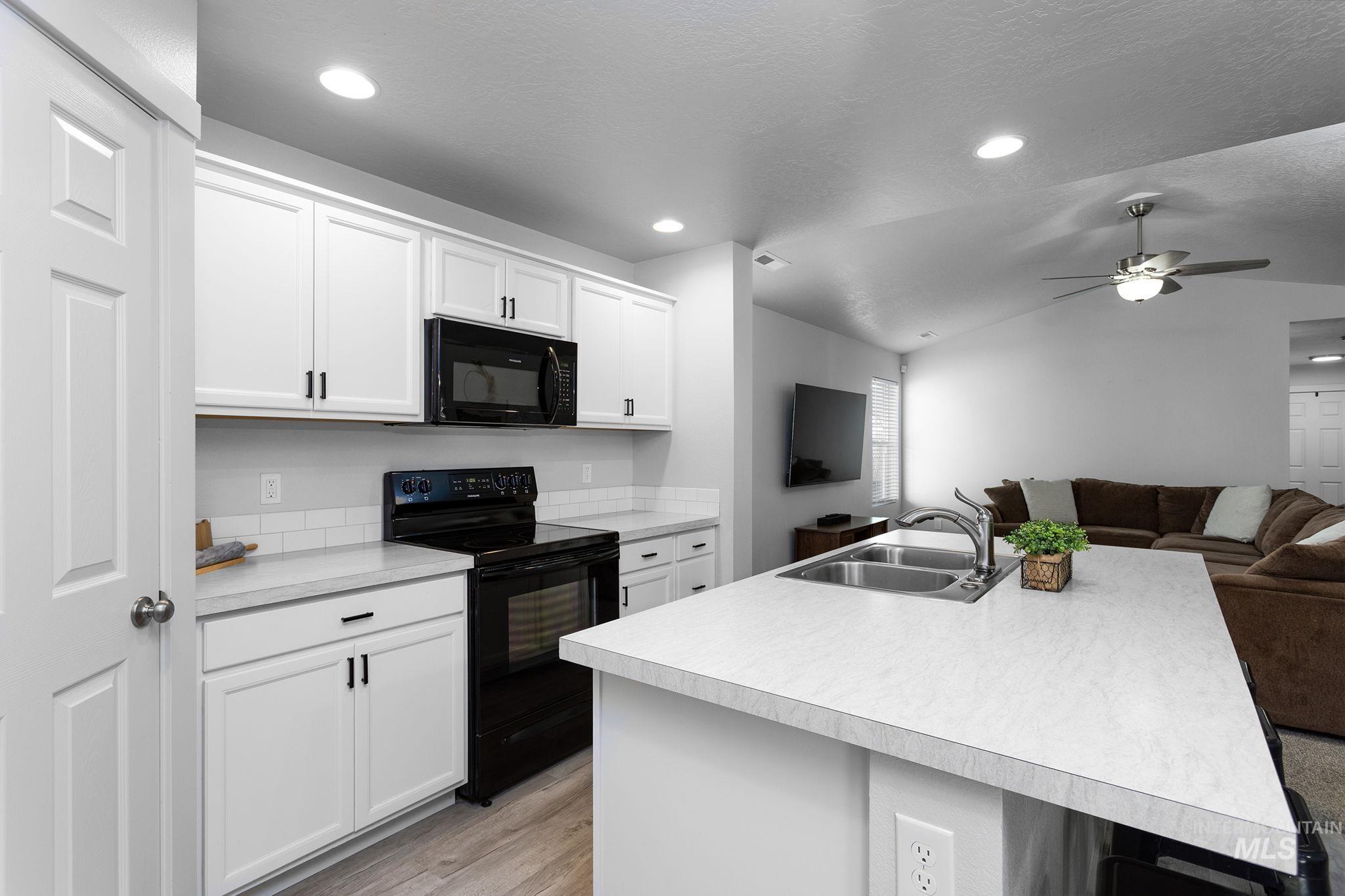 Kitchen with black appliances, open floor plan, a center island with sink, light countertops, and vaulted ceiling