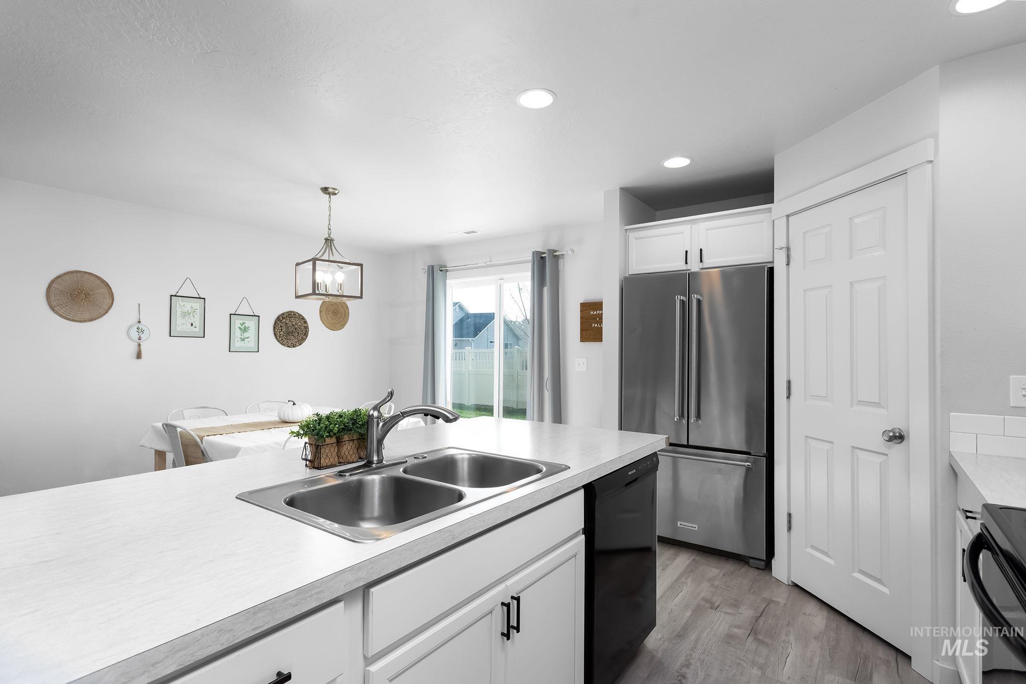 Kitchen featuring black appliances, light countertops, white cabinets, light wood finished floors, and decorative light fixtures