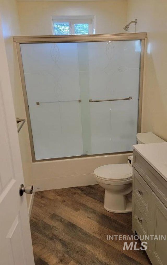 Bathroom with dark wood-style floors, vanity, and combined bath / shower with glass door