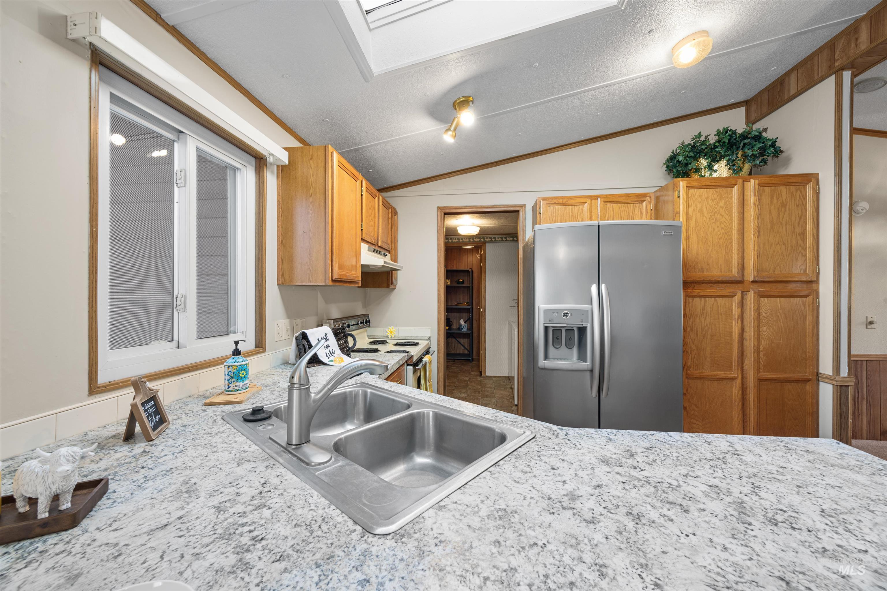 Kitchen featuring stainless steel fridge, light countertops, white range with electric cooktop, vaulted ceiling, and brown cabinets