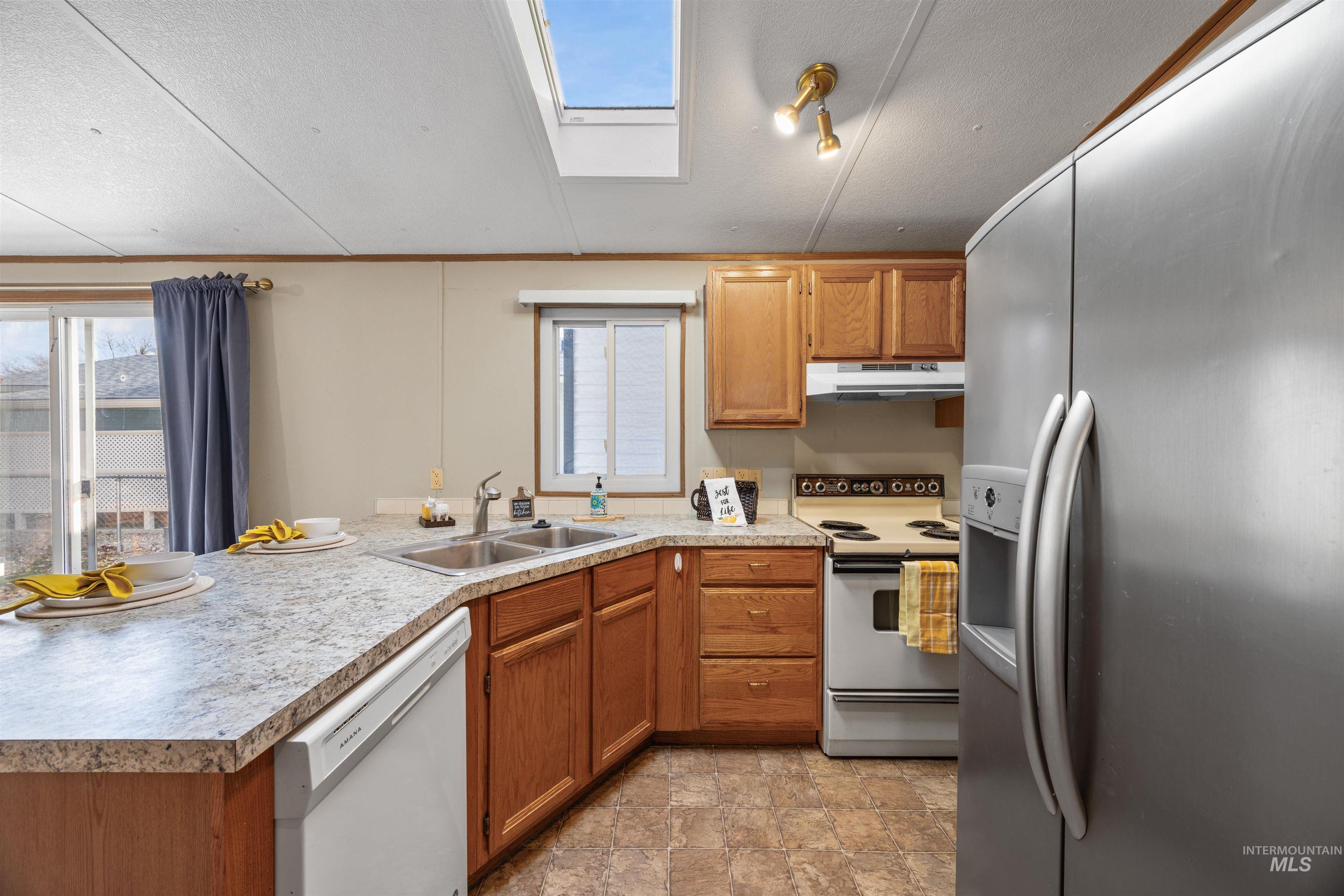 Kitchen with white appliances, light countertops, a skylight, brown cabinetry, and a peninsula