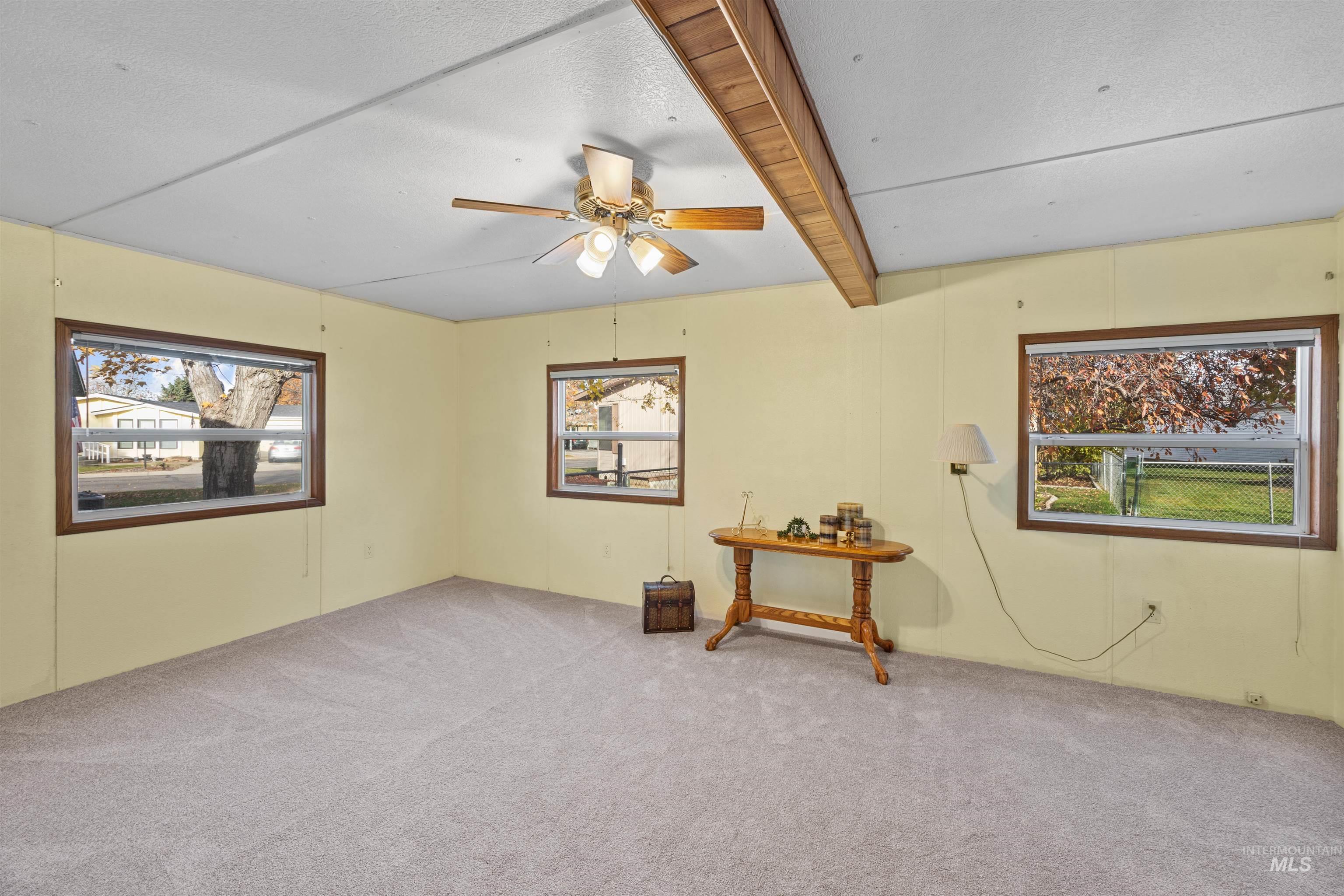 Carpeted primary bedroom featuring spacious windows with lots of light, beam ceiling, and a ceiling fan.