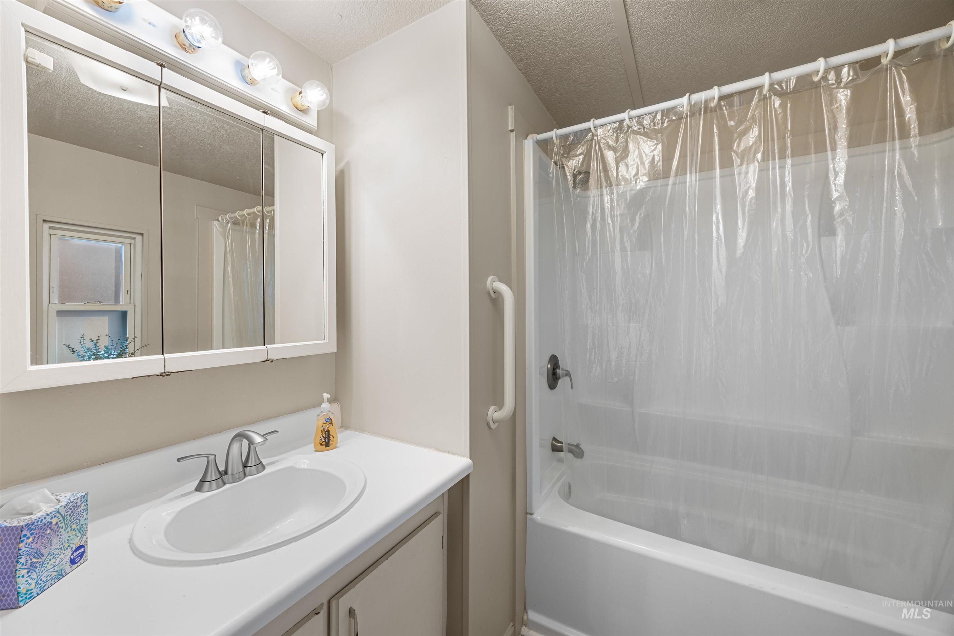 Full bath featuring shower / bathtub combination with curtain, vanity, and a textured ceiling