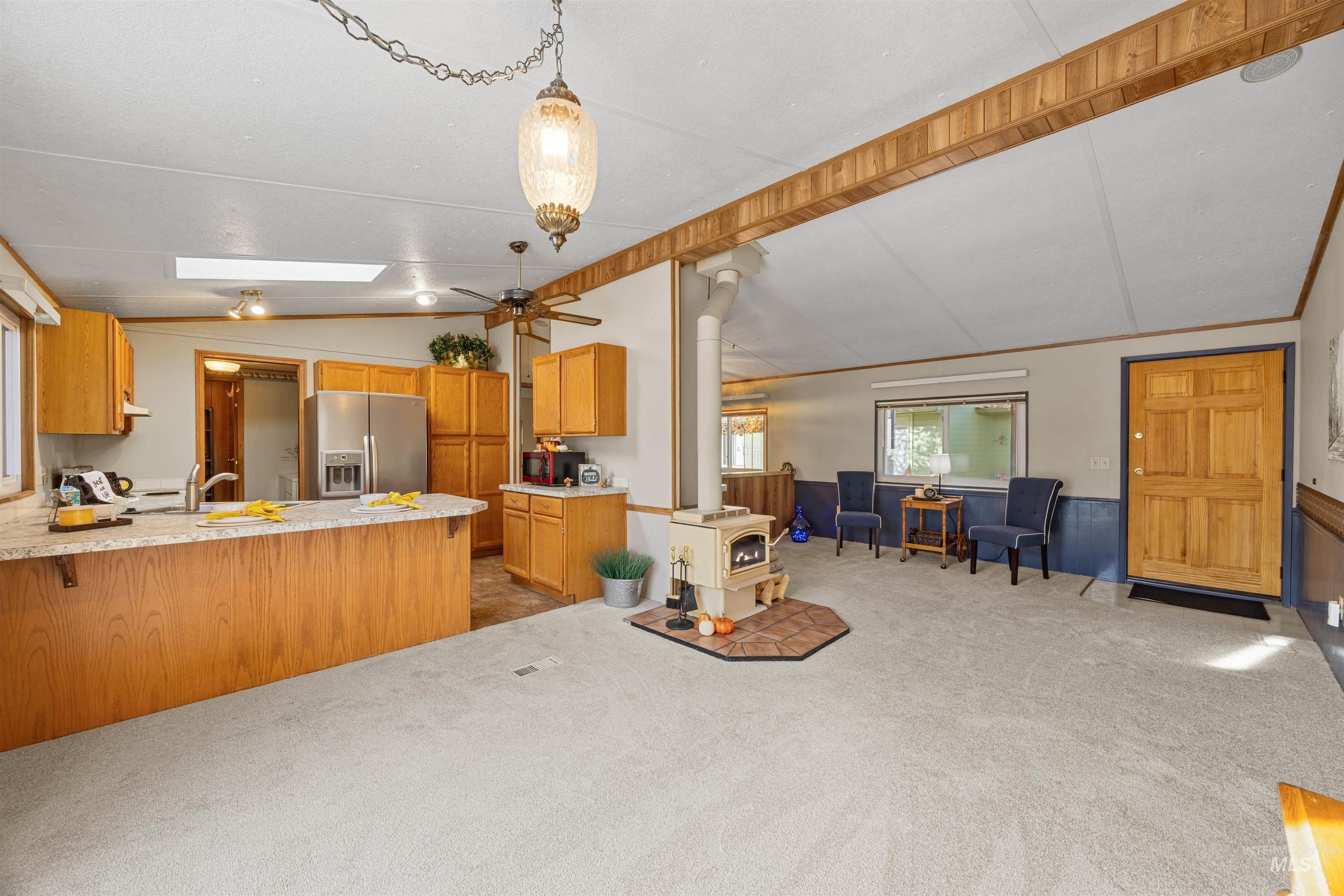 Kitchen with a wood stove, vaulted ceiling, light countertops, open floor plan, and stainless steel fridge with ice dispenser