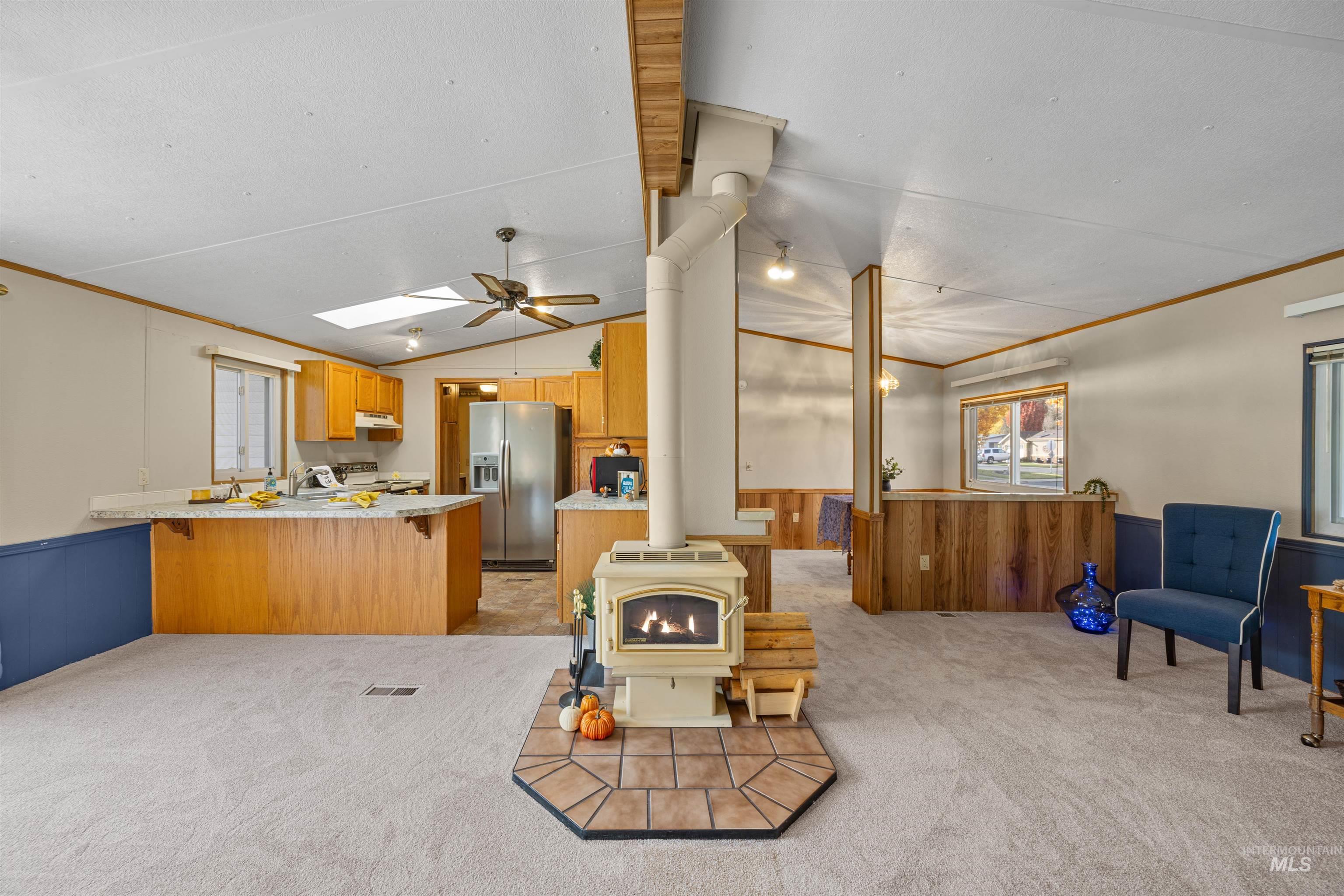 Kitchen with wainscoting, a wood stove, wood walls, ornamental molding, and open floor plan