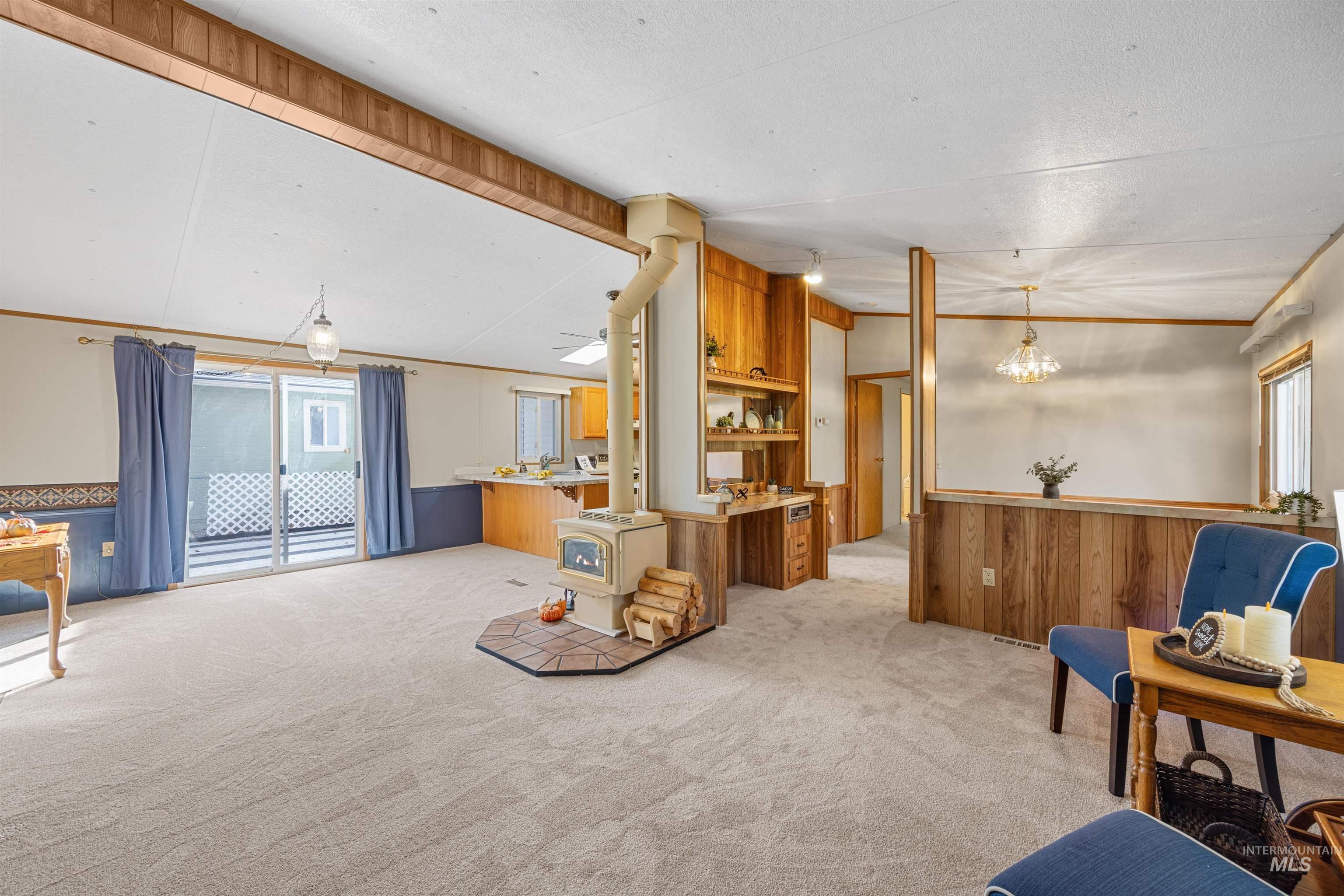 Sitting room with wainscoting, wood walls, a wood stove, light carpet, and crown molding