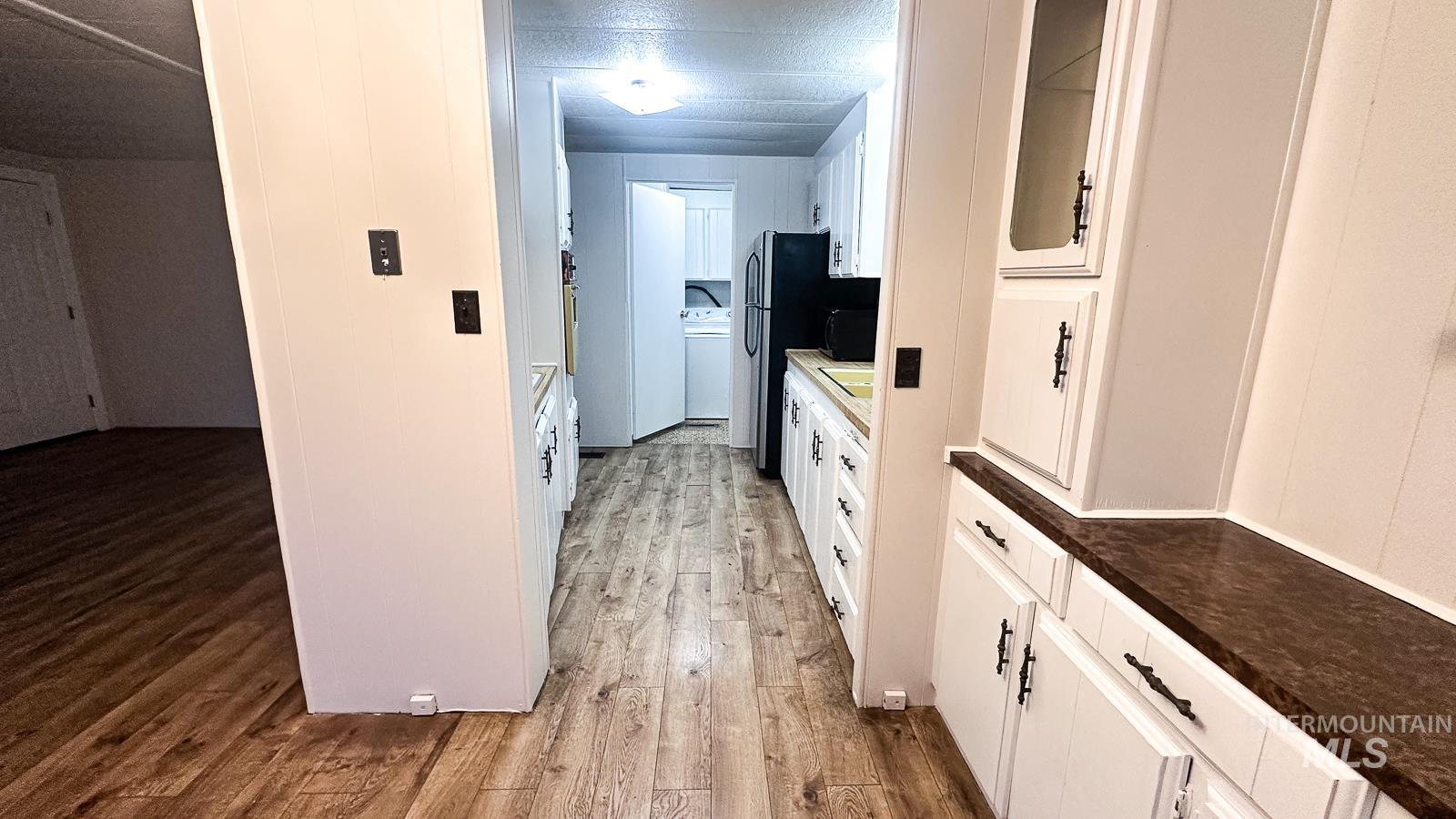 Kitchen with white cabinets, light wood-style floors, glass insert cabinets, dark countertops, and black microwave