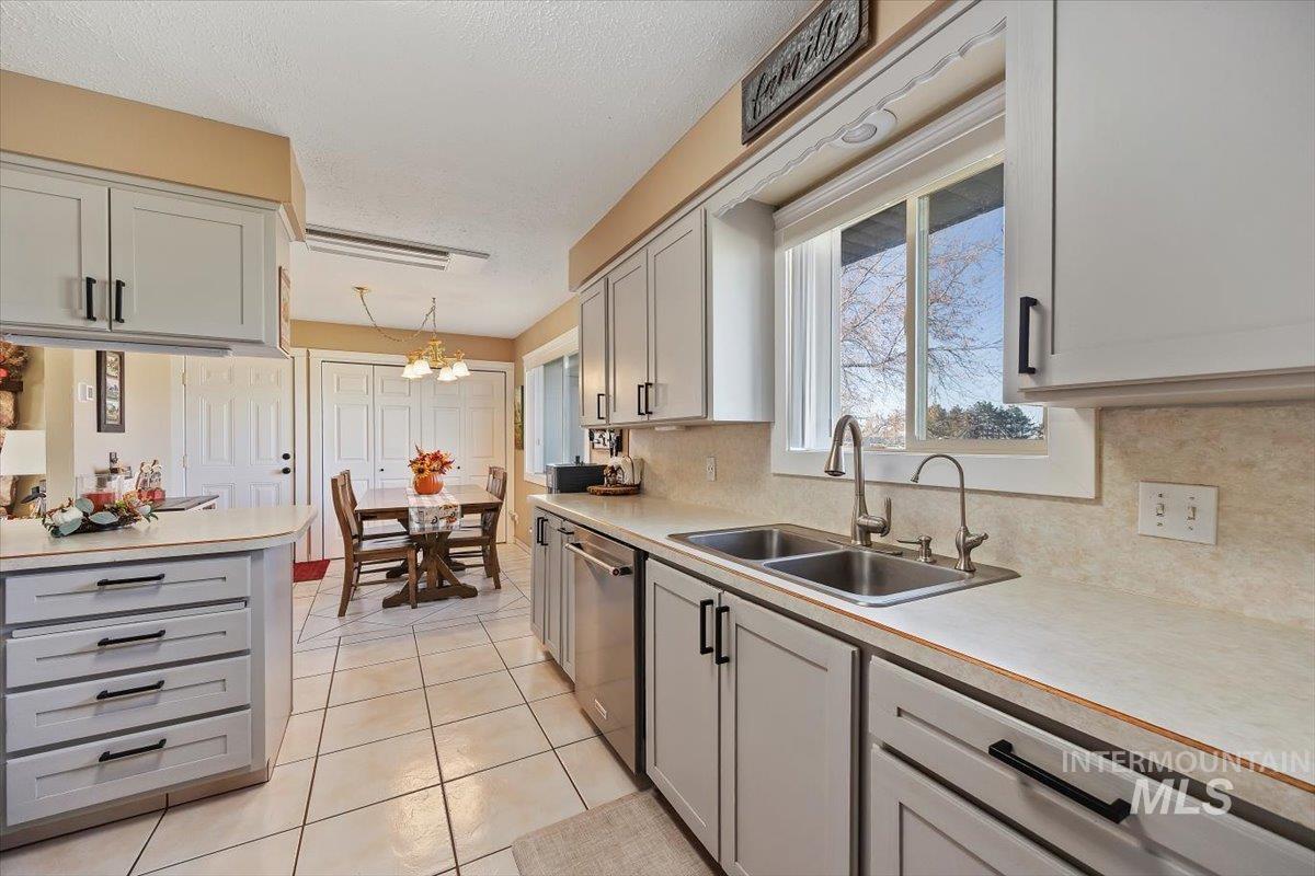 Kitchen featuring gray cabinetry, light countertops, a chandelier, light tile patterned flooring, and a textured ceiling
