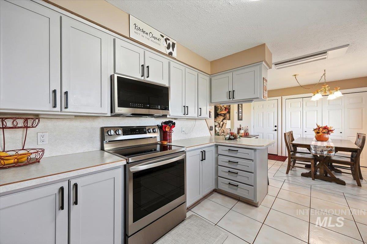 Kitchen with stainless steel appliances, a peninsula, a textured ceiling, light countertops, and light tile patterned floors