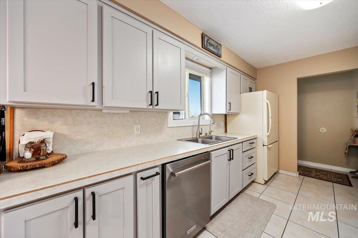 Kitchen featuring light countertops, stainless steel dishwasher, a textured ceiling, light tile patterned floors, and tasteful backsplash