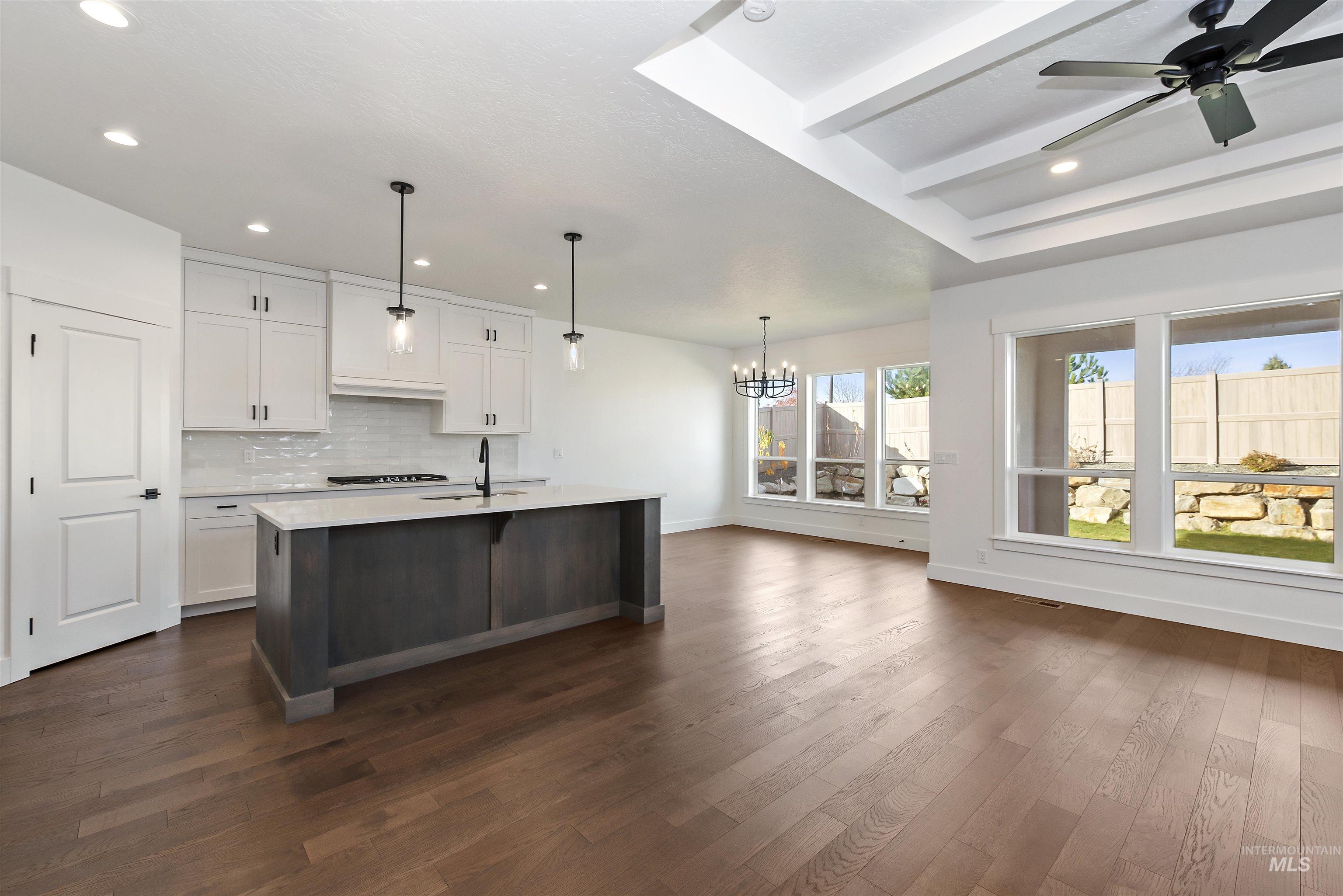 Kitchen with white cabinetry, decorative backsplash, decorative light fixtures, a chandelier, and a kitchen island with sink