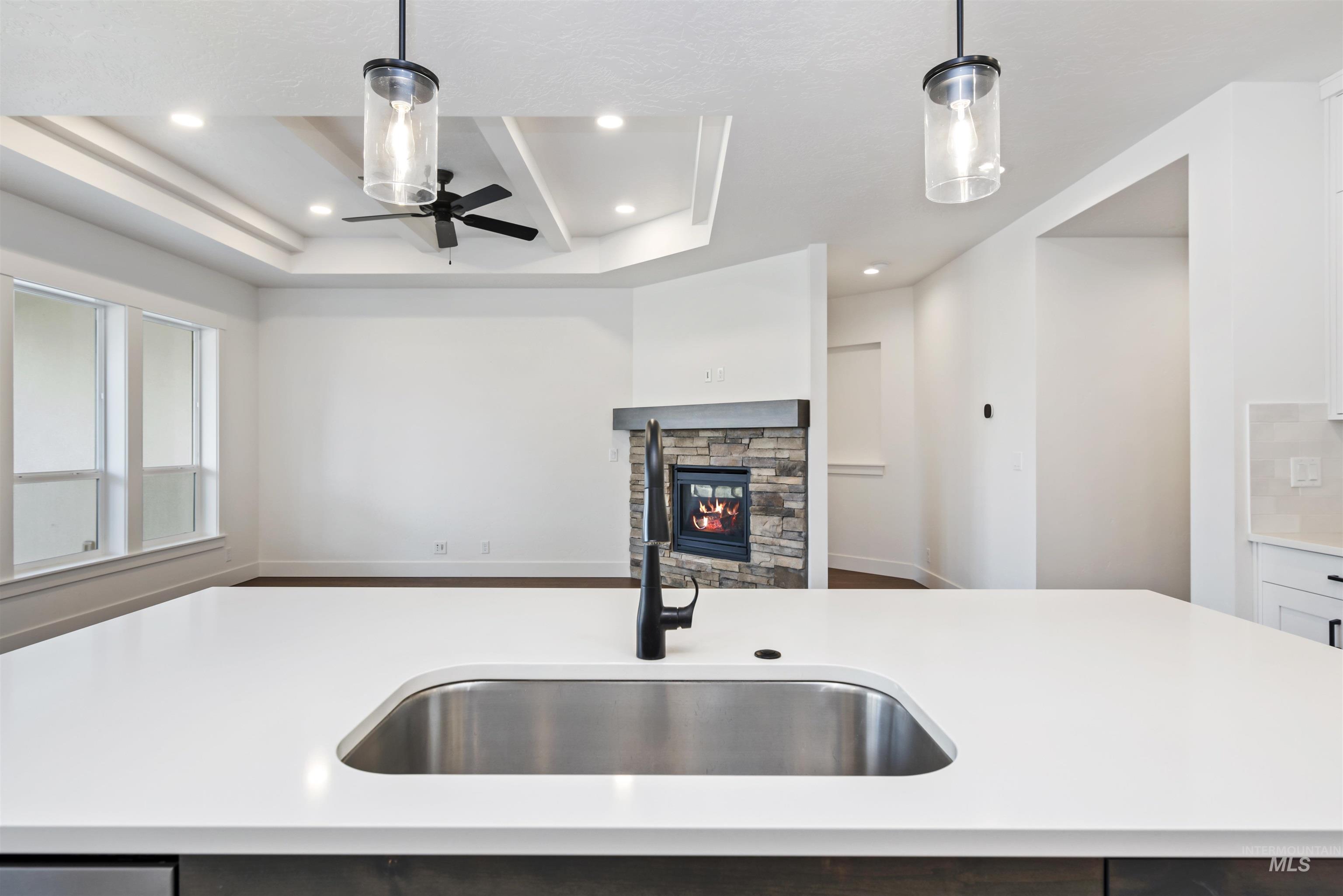 Kitchen featuring open floor plan, decorative light fixtures, a raised ceiling, a stone fireplace, and recessed lighting