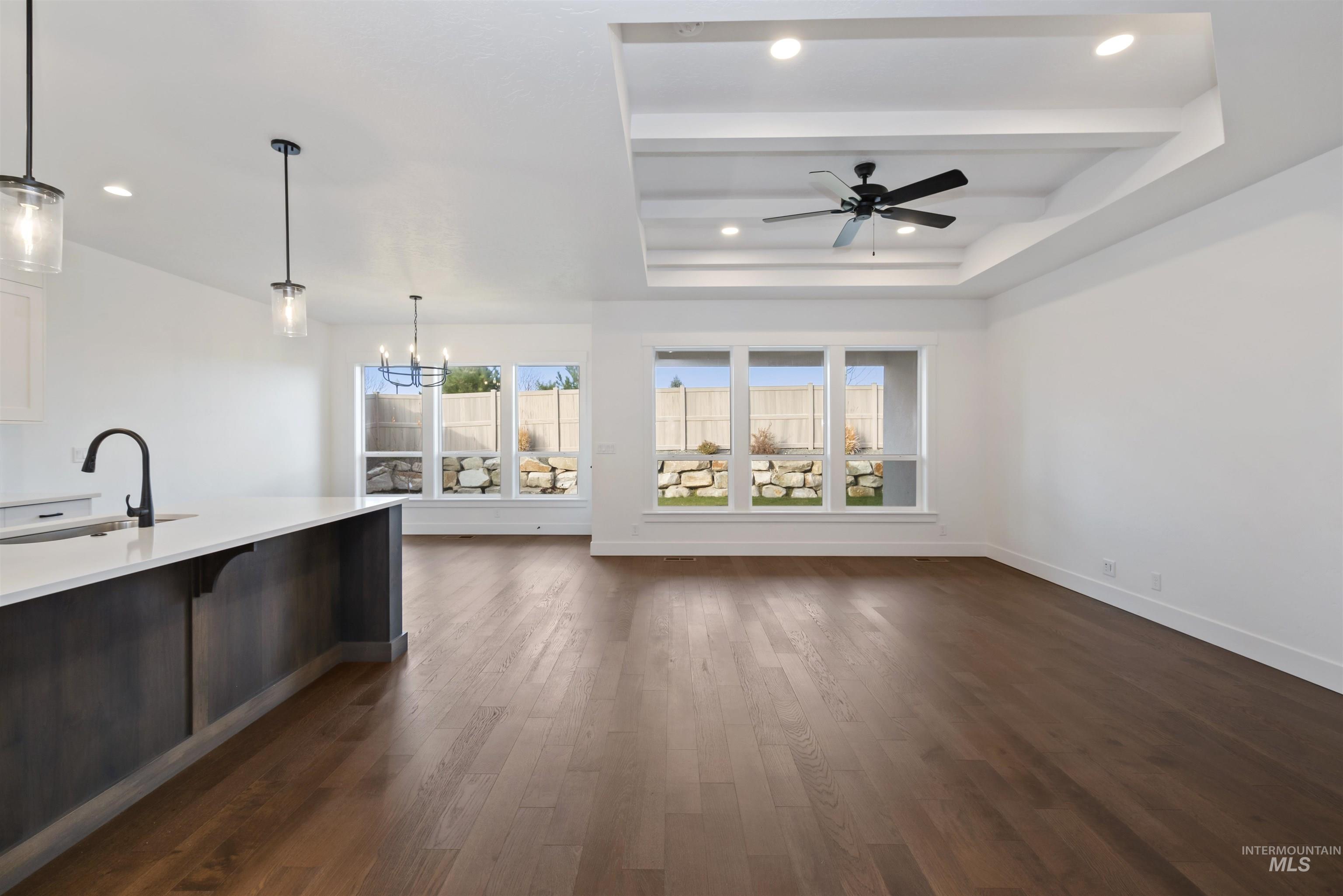 Unfurnished living room featuring a raised ceiling, dark wood-type flooring, a chandelier, ceiling fan, and beamed ceiling