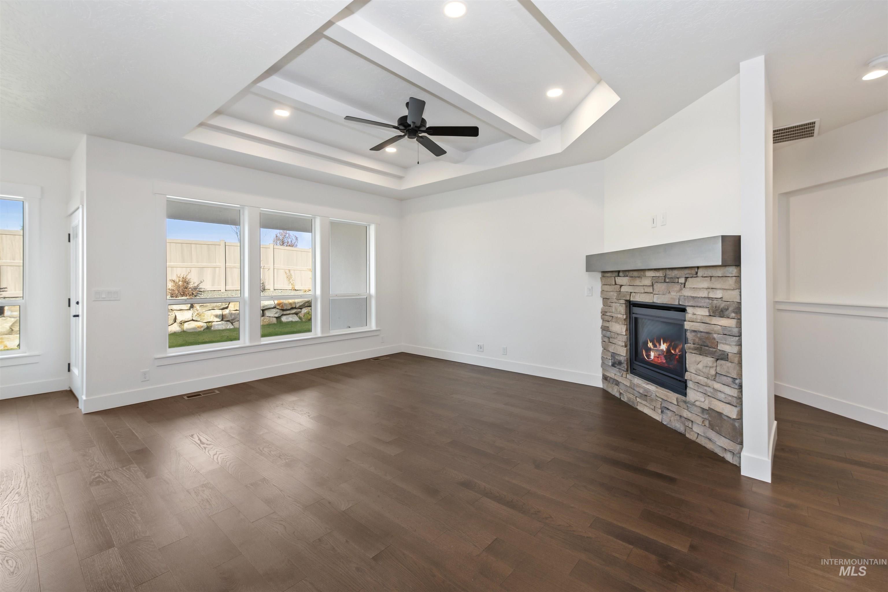 Unfurnished living room with a raised ceiling, dark wood-type flooring, a stone fireplace, and recessed lighting