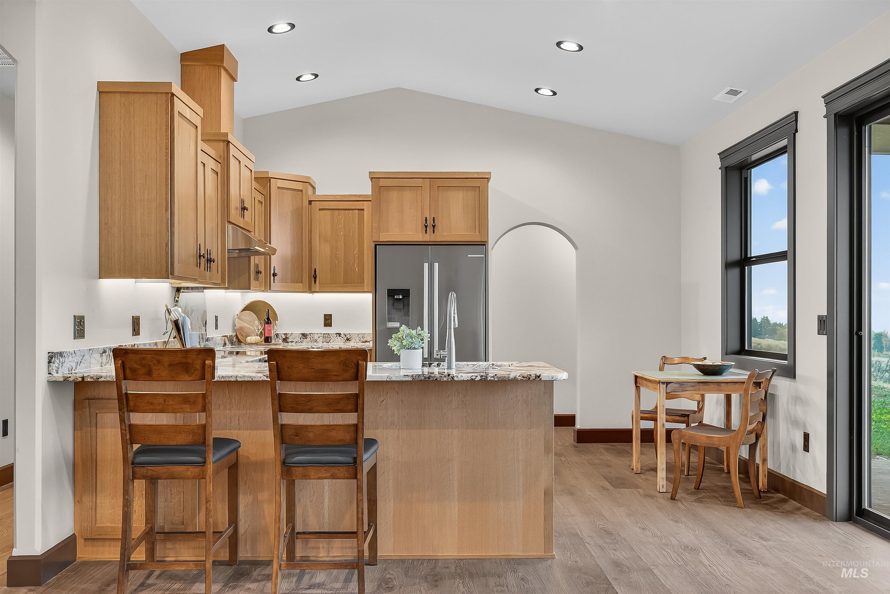 Kitchen with light stone counters, stainless steel refrigerator with ice dispenser, light wood finished floors, a peninsula, and arched walkways