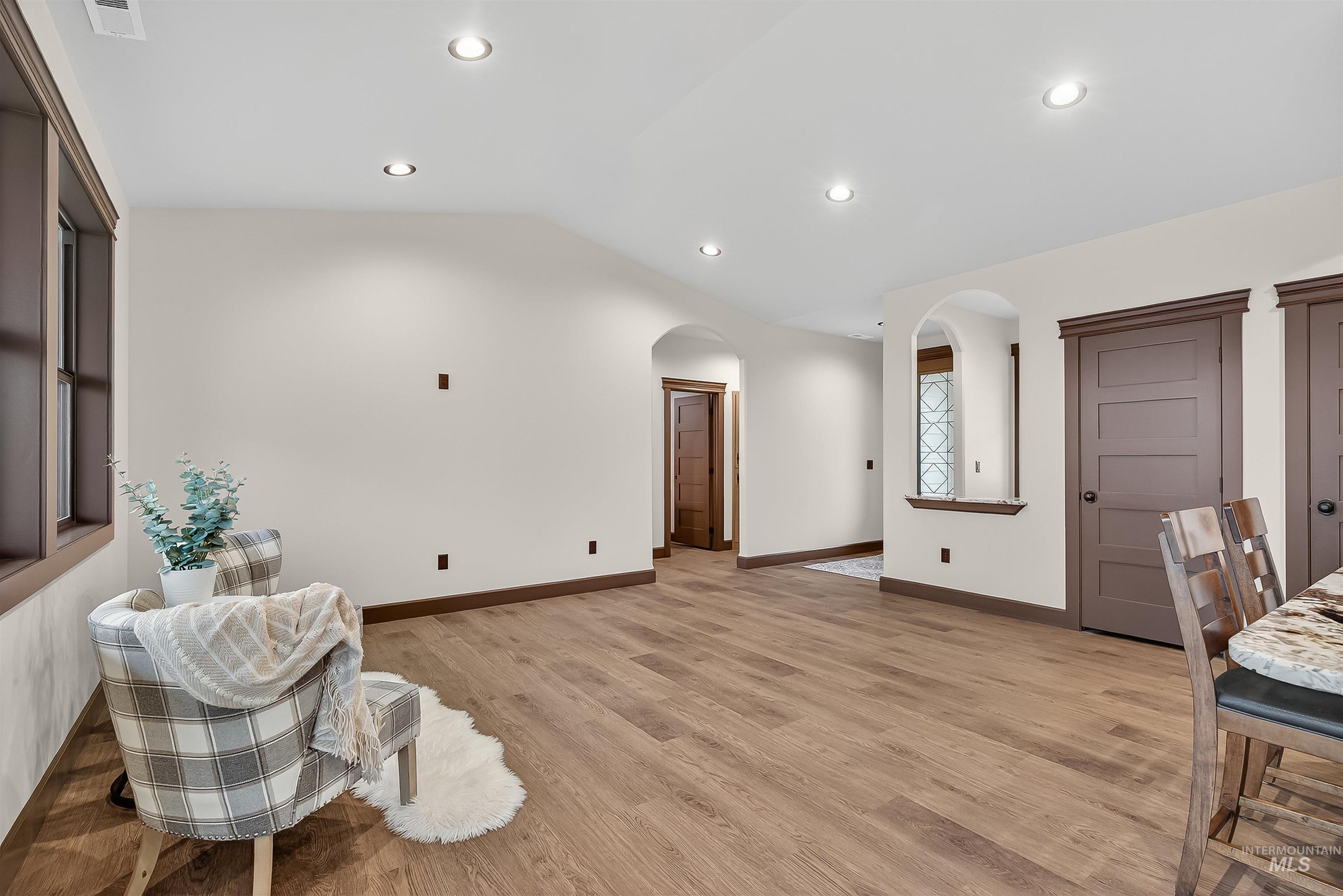 Living area with light wood-style flooring, lofted ceiling, arched walkways, and recessed lighting