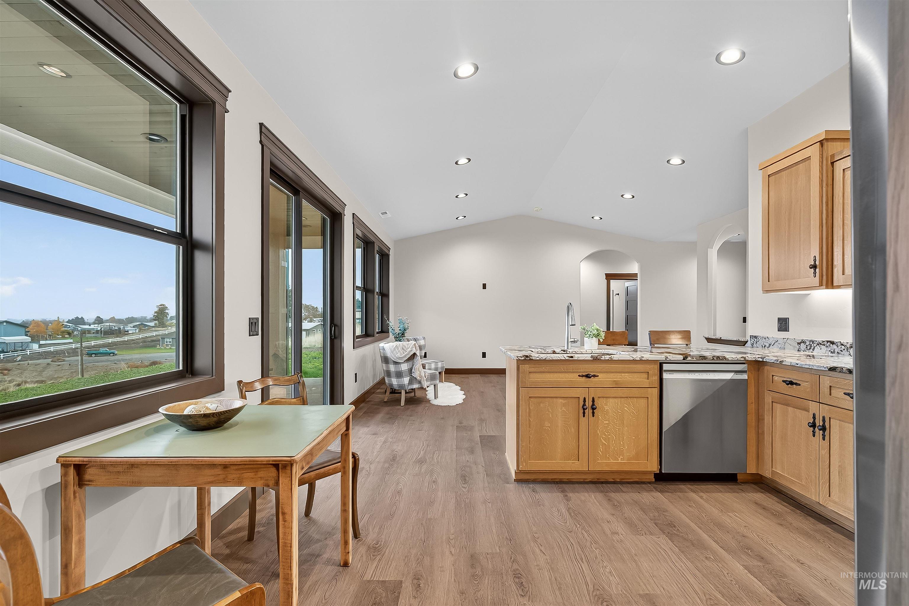 Kitchen with vaulted ceiling, light stone countertops, light wood-style flooring, stainless steel dishwasher, and a peninsula