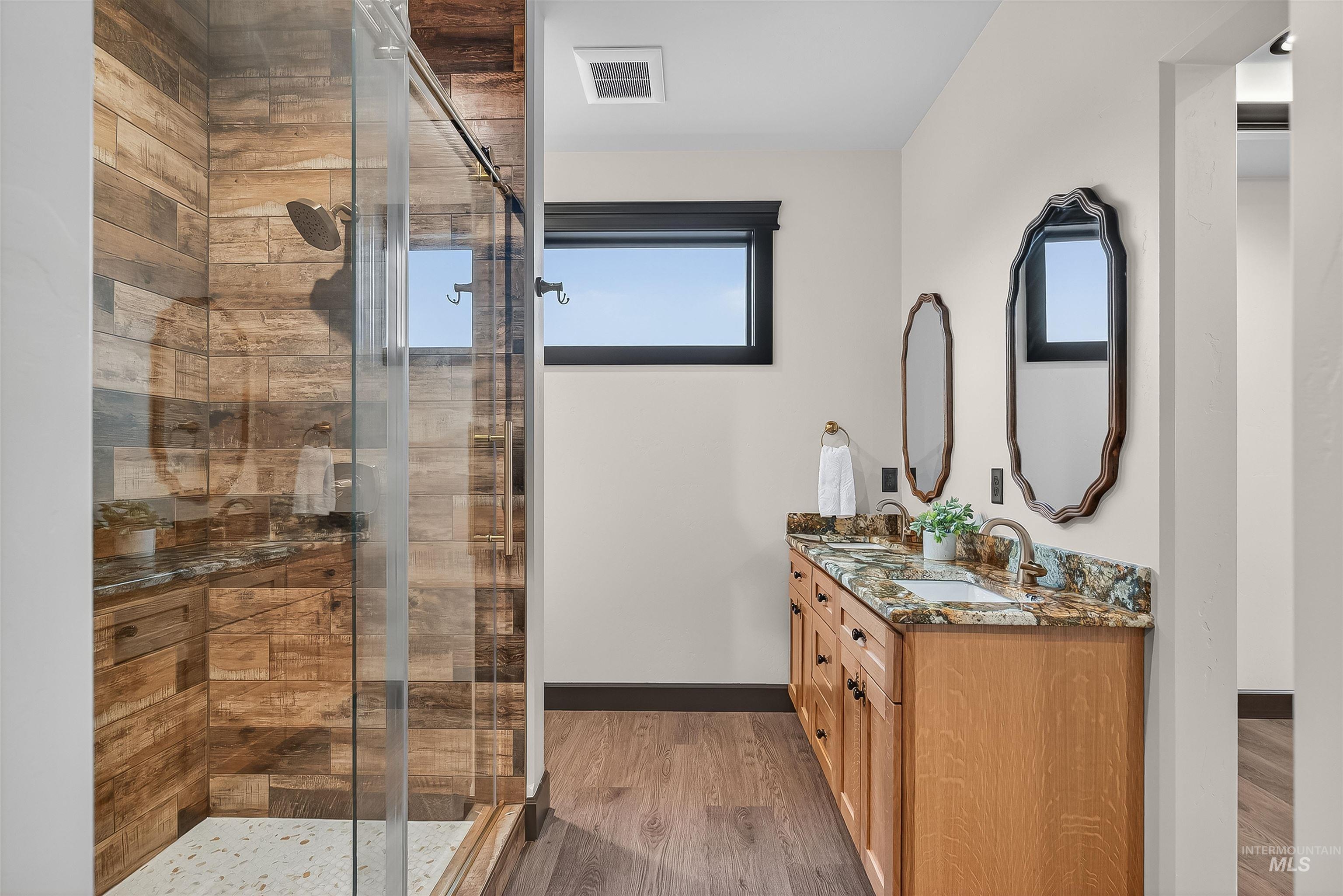 Full bath featuring light wood-style flooring, double vanity, and a stall shower