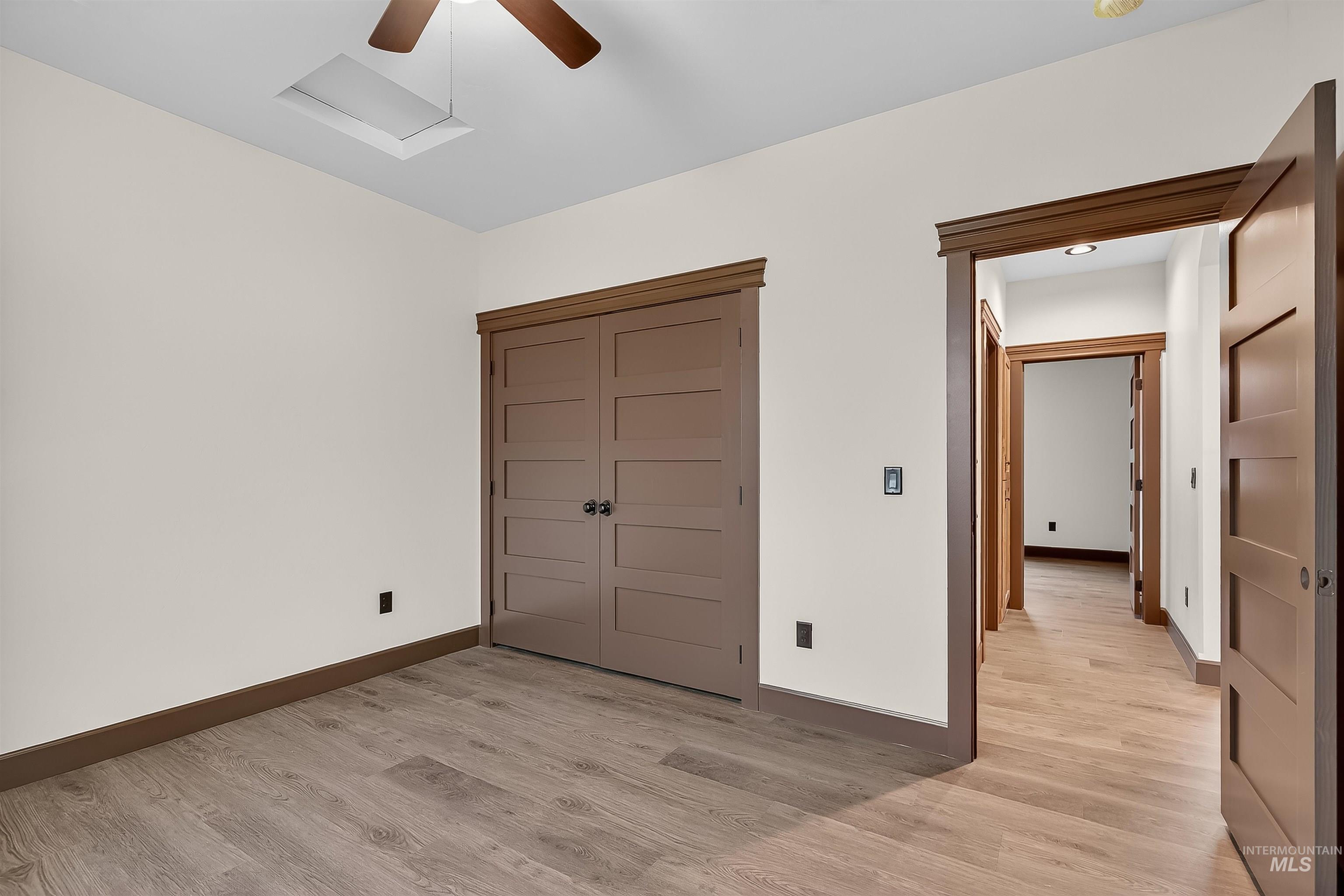 Unfurnished bedroom with a closet, attic access, light wood-style floors, and a ceiling fan