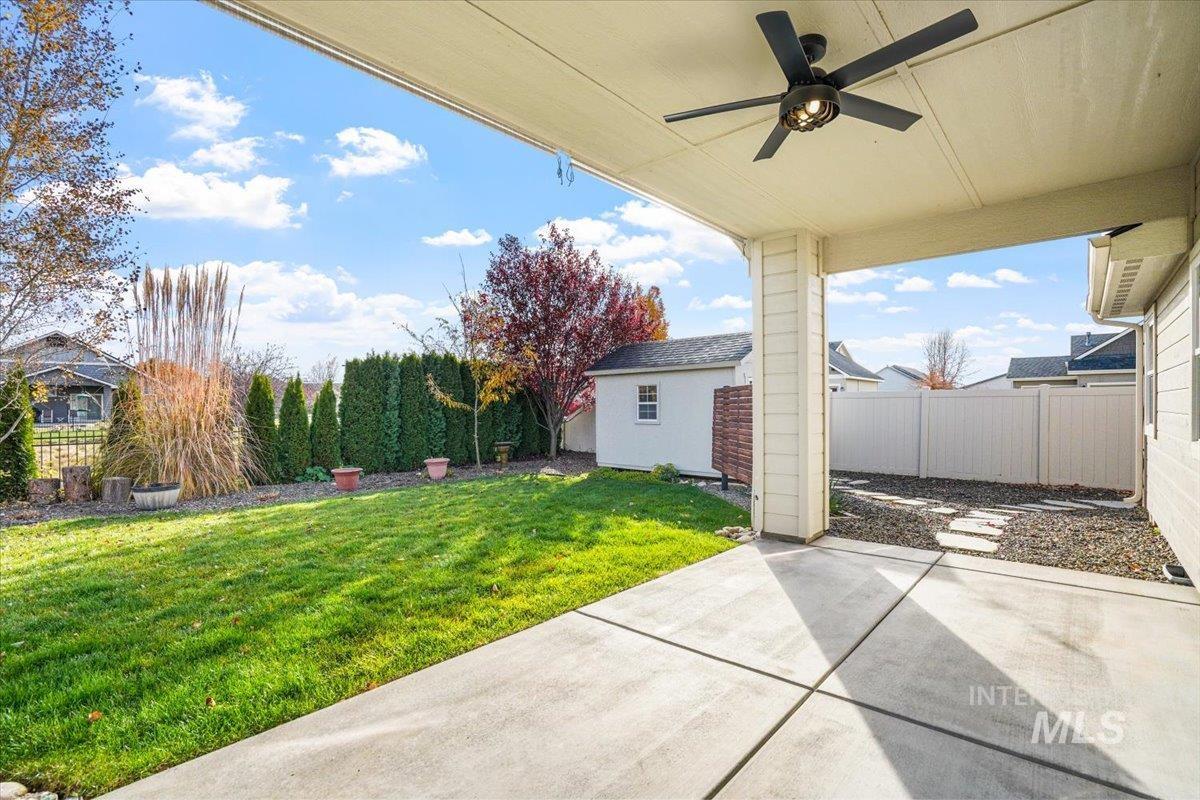 Fenced backyard with a patio, a ceiling fan, and an outbuilding
