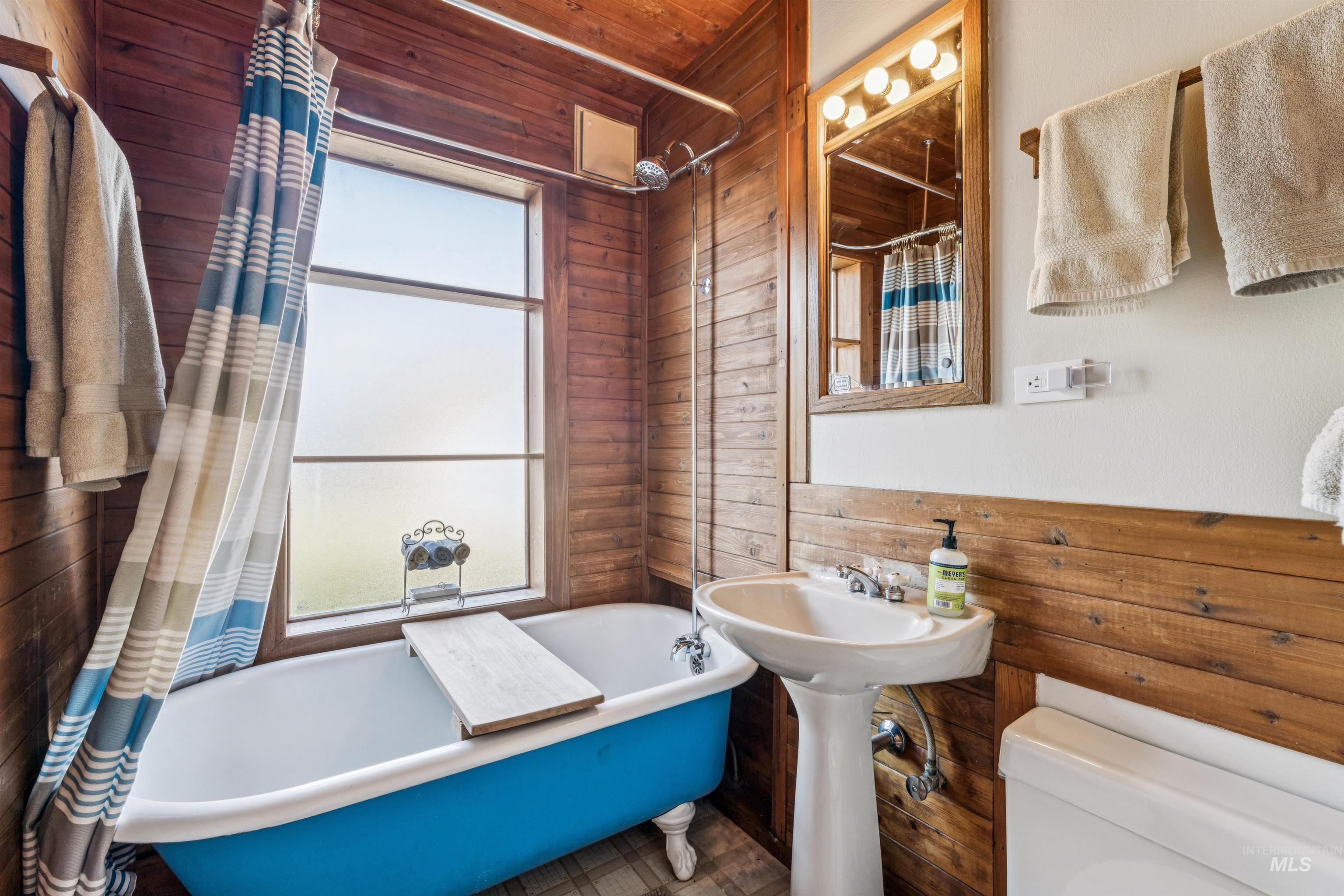 Full bath featuring wooden walls and a combined bath / shower with freestanding tub