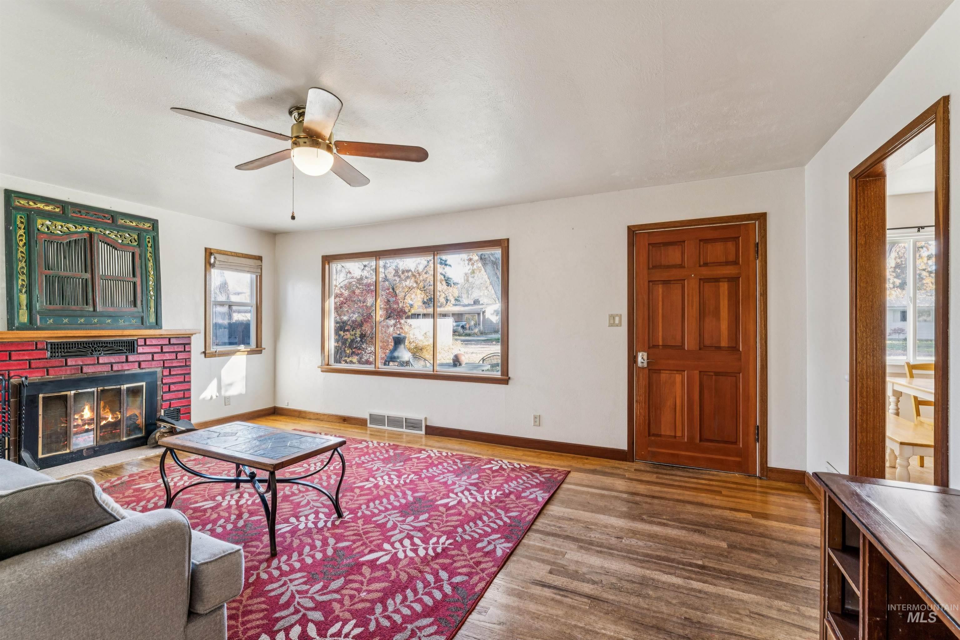 Living area featuring plenty of natural light, wood finished floors, a brick fireplace, and a ceiling fan