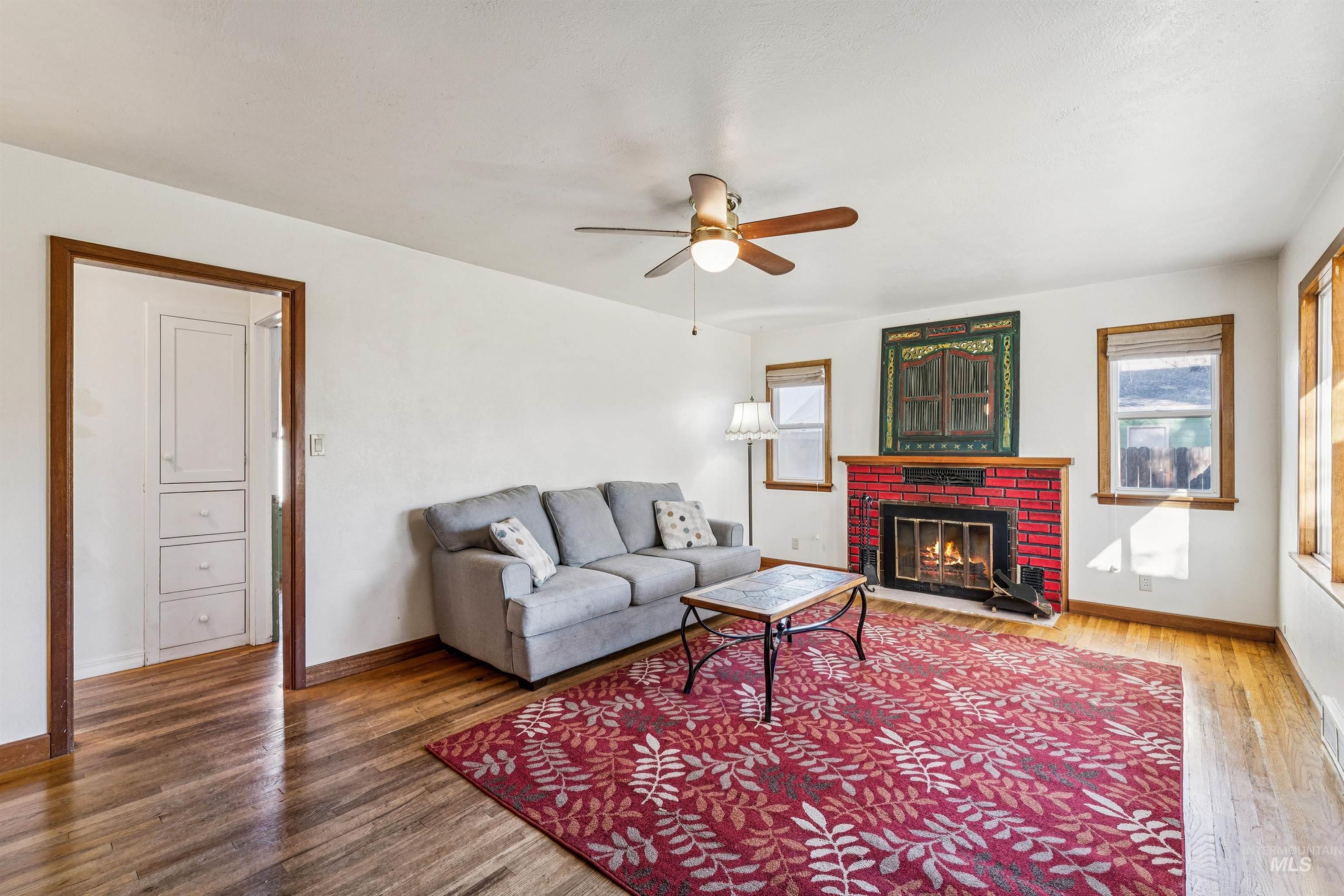 Living area featuring a brick fireplace, ceiling fan, and wood finished floors