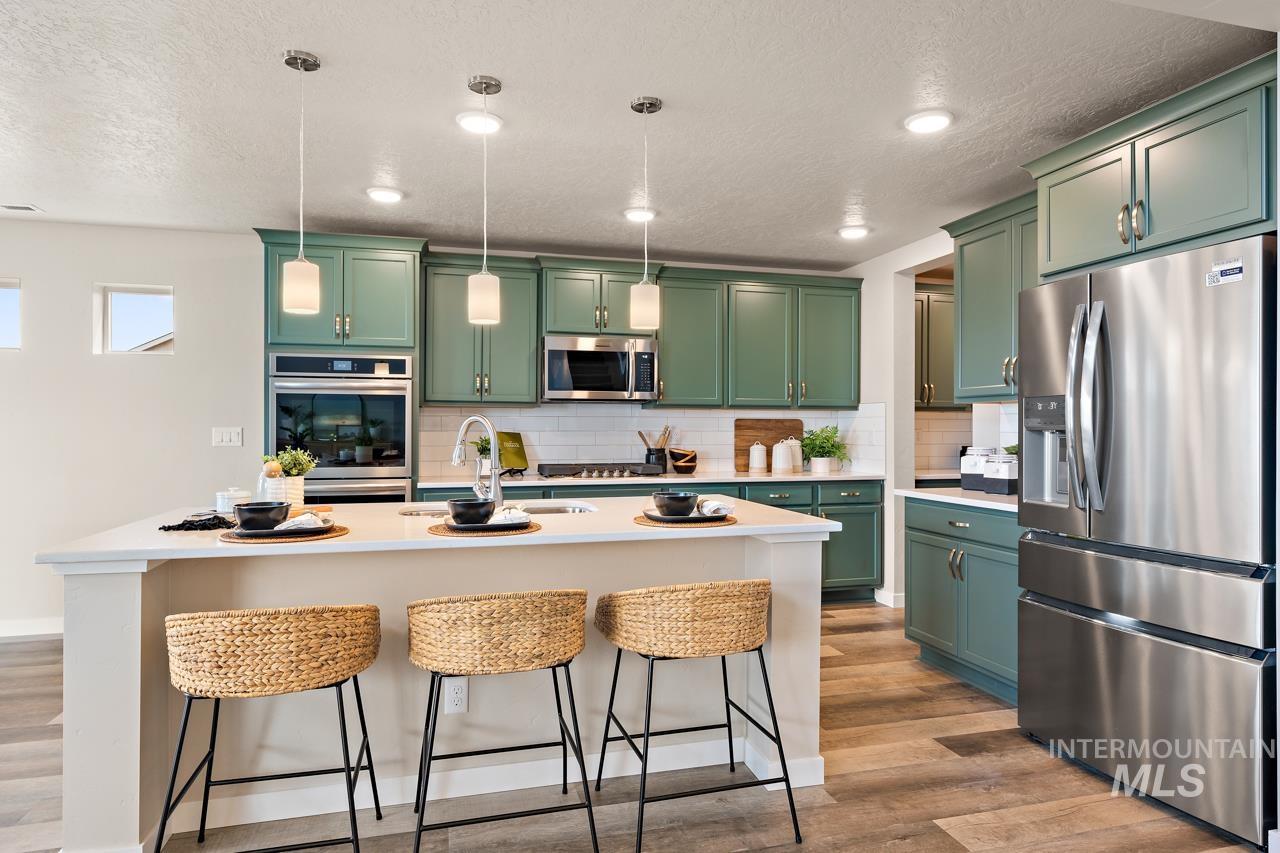 Kitchen with green cabinets, stainless steel appliances, backsplash, a kitchen bar, and wood finished floors