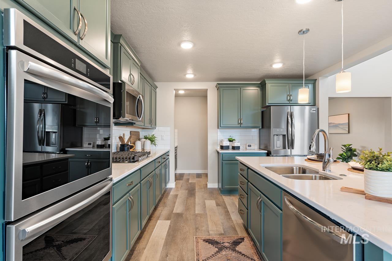 Kitchen with appliances with stainless steel finishes, light wood-style flooring, light countertops, decorative light fixtures, and a textured ceiling