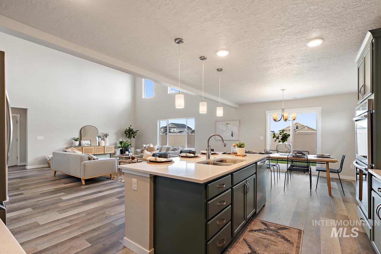 Kitchen featuring a textured ceiling, wood finished floors, light countertops, a center island with sink, and hanging light fixtures