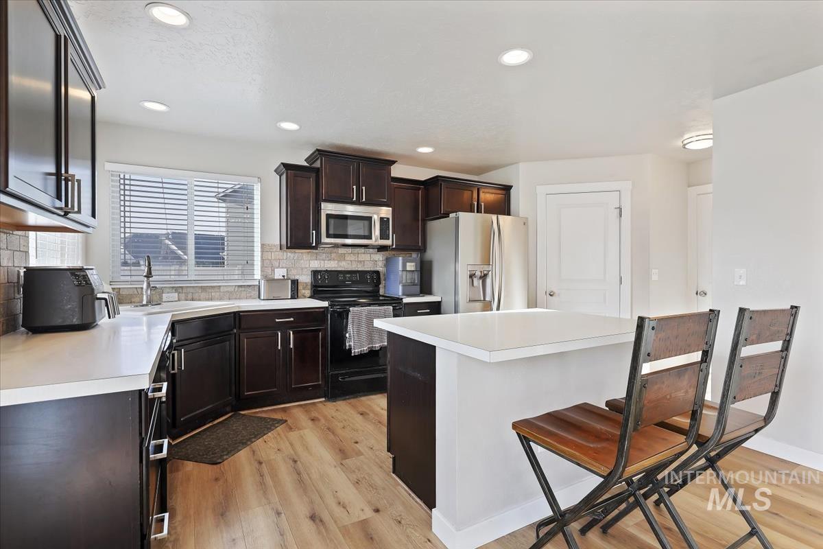 Kitchen with appliances with stainless steel finishes, a breakfast bar, light countertops, light wood-style floors, and recessed lighting
