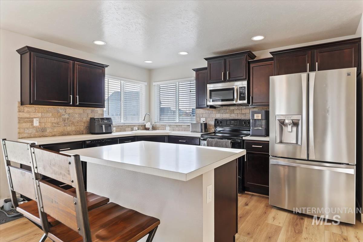 Kitchen with stainless steel appliances, a breakfast bar, dark brown cabinetry, a center island, and light countertops