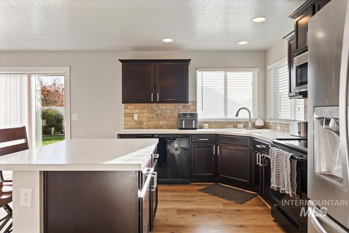Kitchen featuring dark brown cabinetry, black appliances, light wood finished floors, recessed lighting, and tasteful backsplash