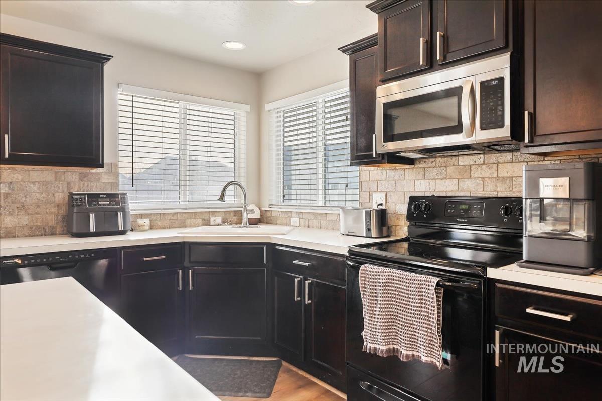 Kitchen with black electric range oven, decorative backsplash, stainless steel microwave, light countertops, and recessed lighting