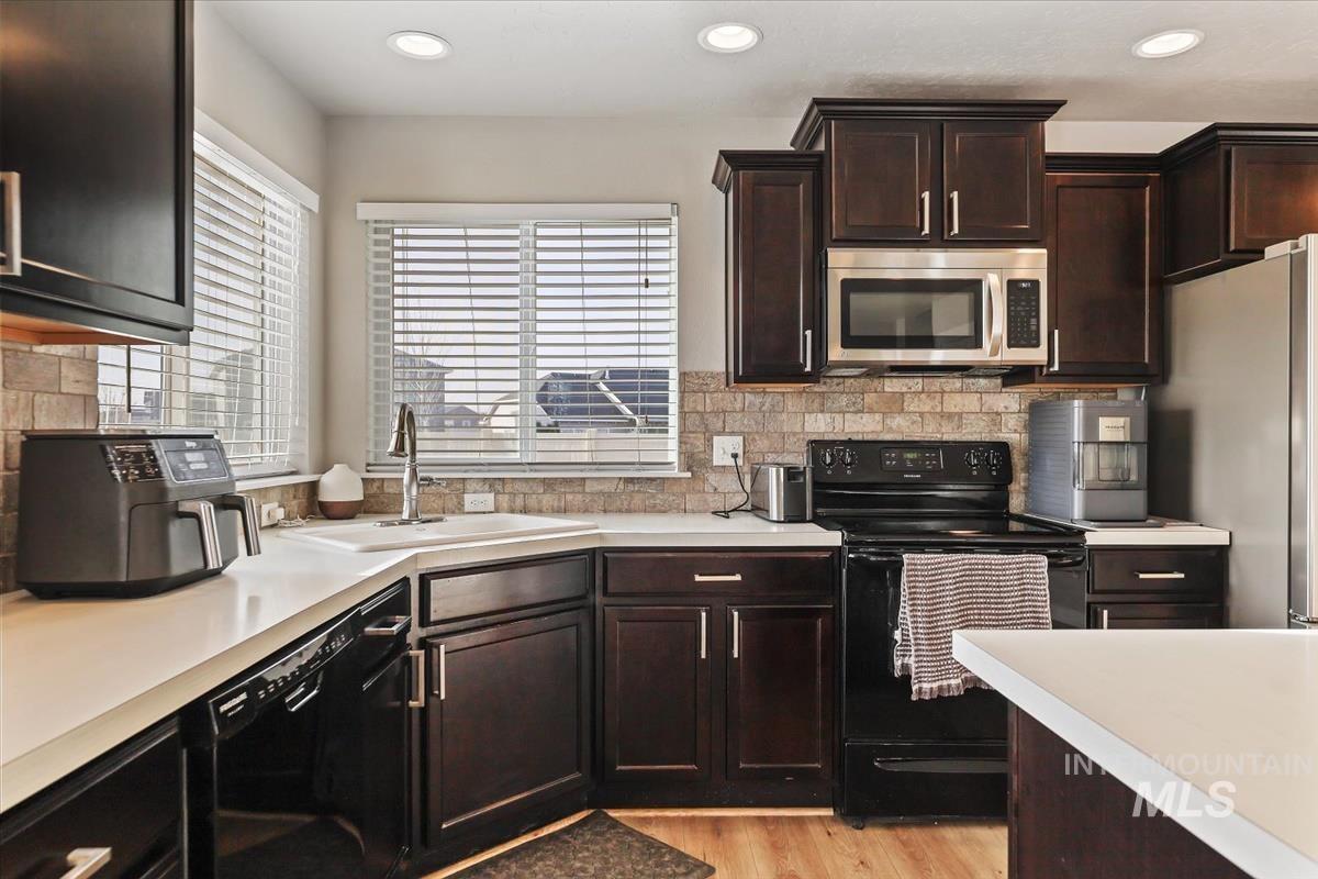 Kitchen with black appliances, light countertops, recessed lighting, dark brown cabinets, and light wood-type flooring