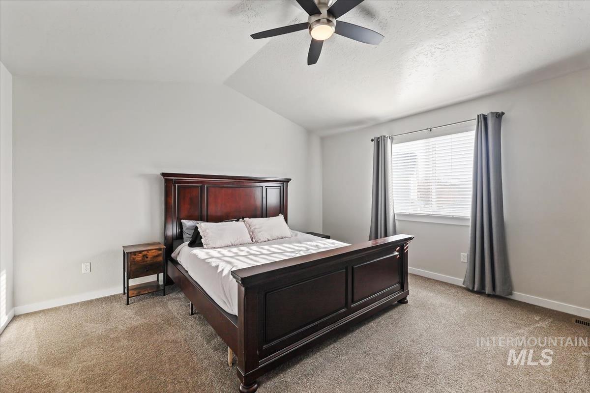 Bedroom with vaulted ceiling, light carpet, ceiling fan, and a textured ceiling