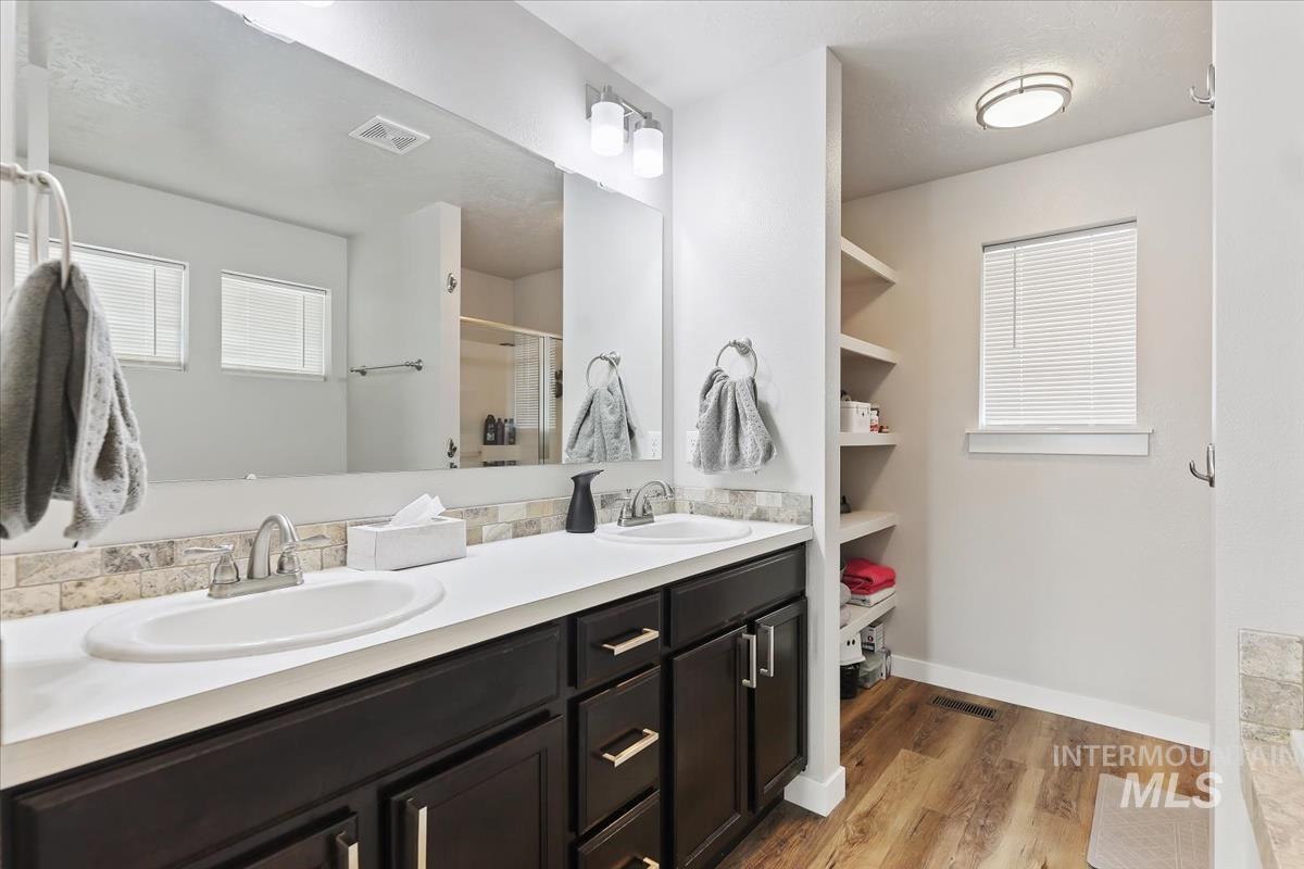 Full bath with double vanity, light wood-style flooring, and a shower stall