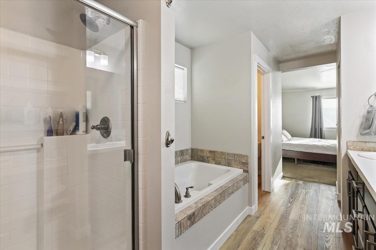 Ensuite bathroom with plenty of natural light, vanity, wood finished floors, and a bath