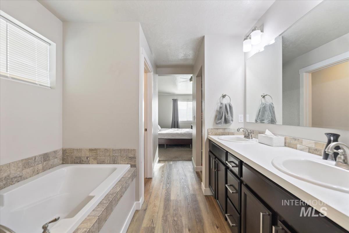 Bathroom featuring double vanity, light wood-style flooring, a garden tub, ensuite bath, and ceiling fan