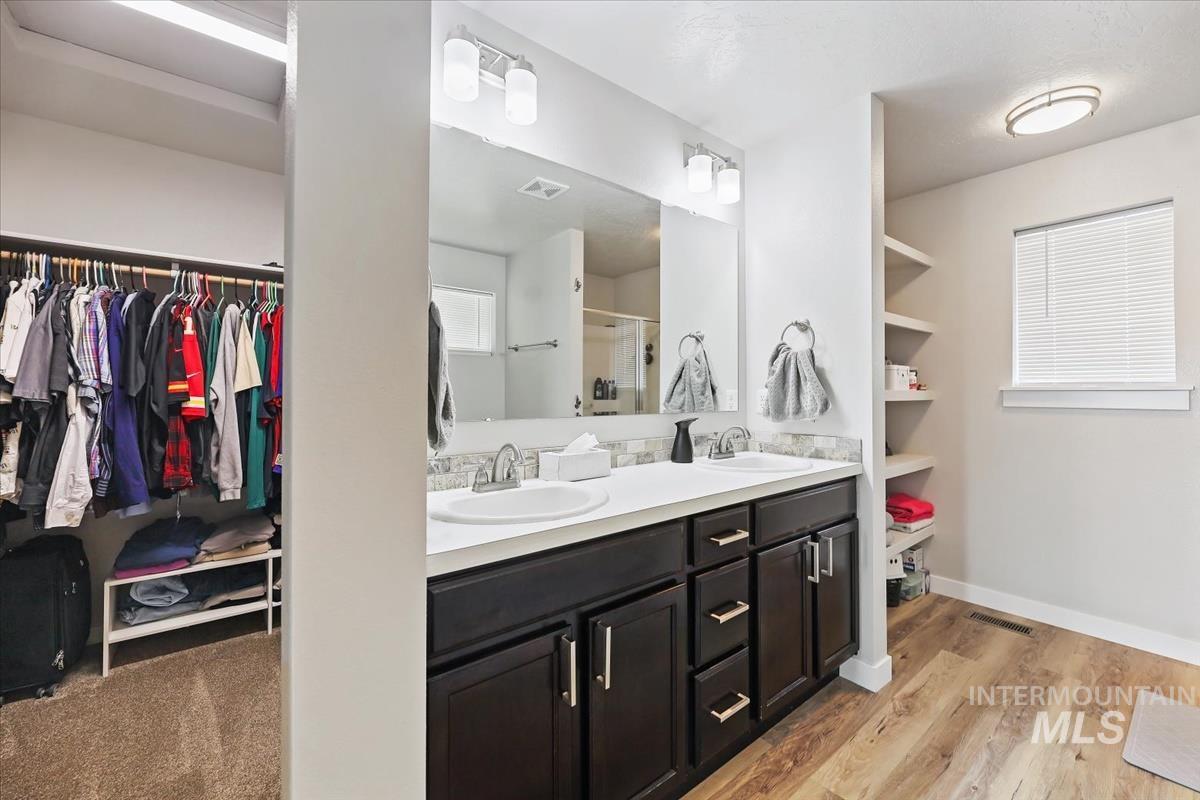 Bathroom featuring a spacious closet, double vanity, a stall shower, and light wood-type flooring
