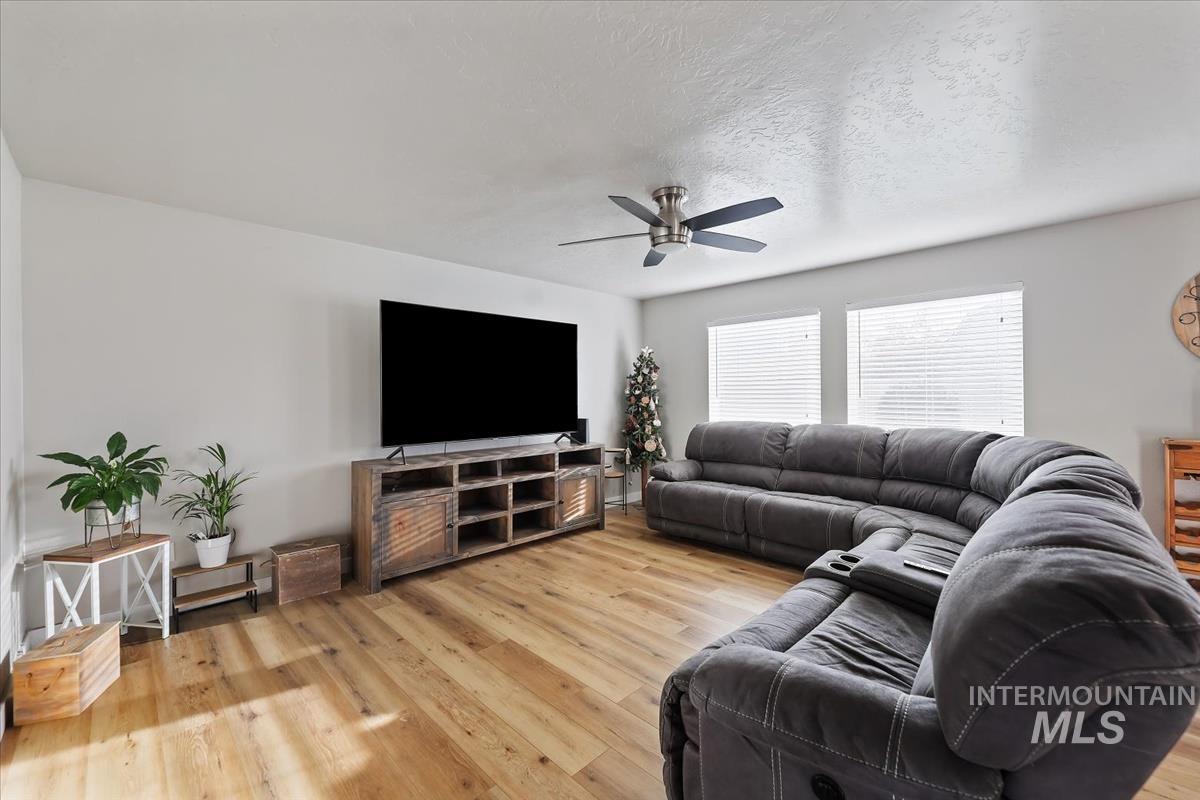 Living room with light wood finished floors, ceiling fan, and a textured ceiling