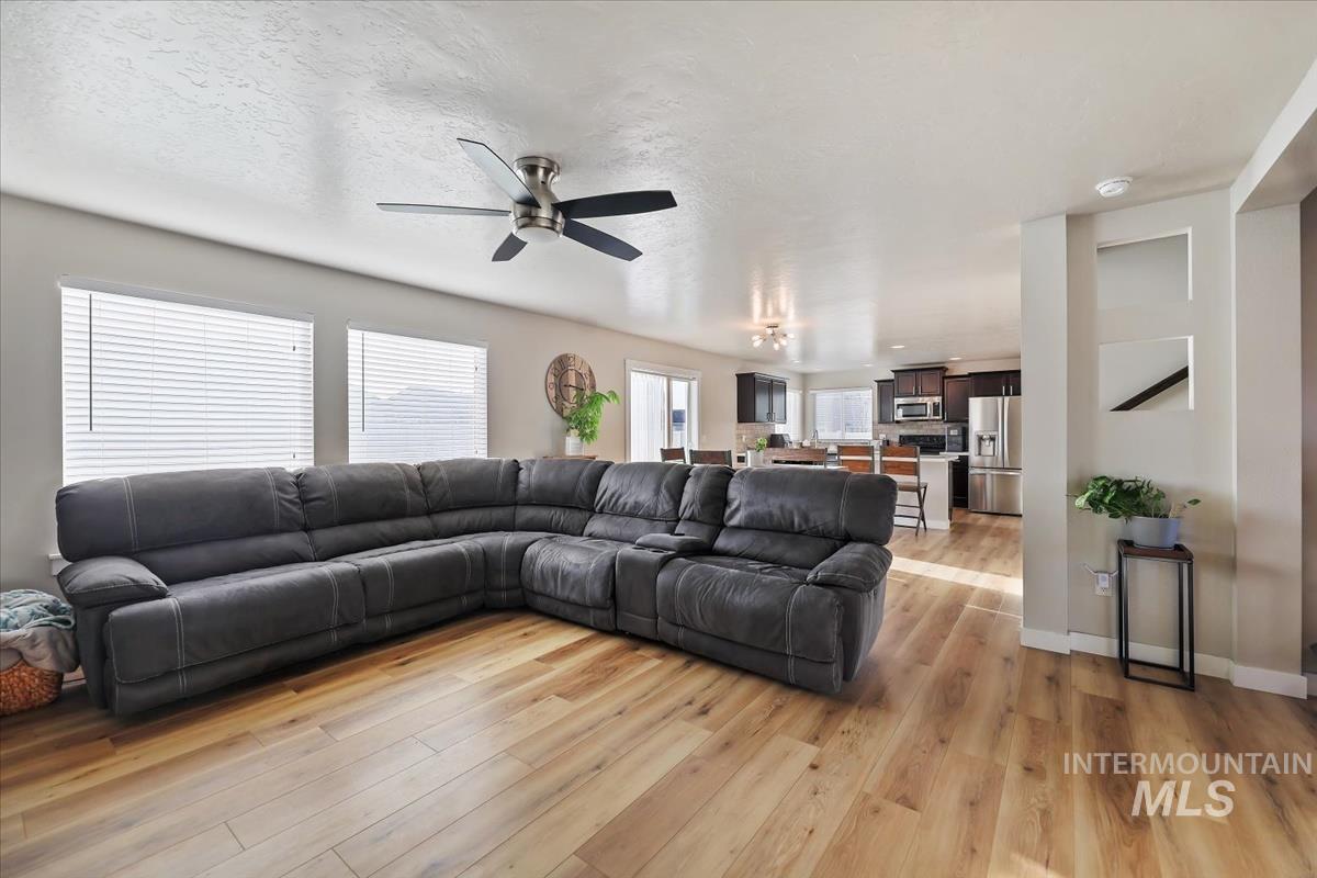 Living area with light wood finished floors, ceiling fan, and a textured ceiling